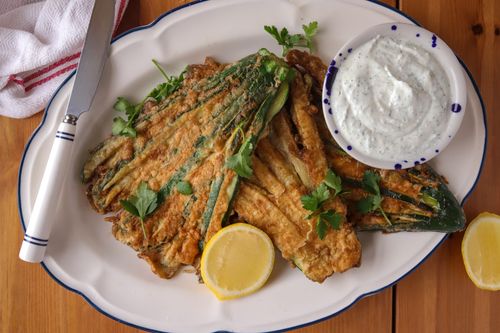 Close-up of golden fried zucchini fans with herby feta dip and lemon wedges on a serving platter – a seasonal veggie side made simple.