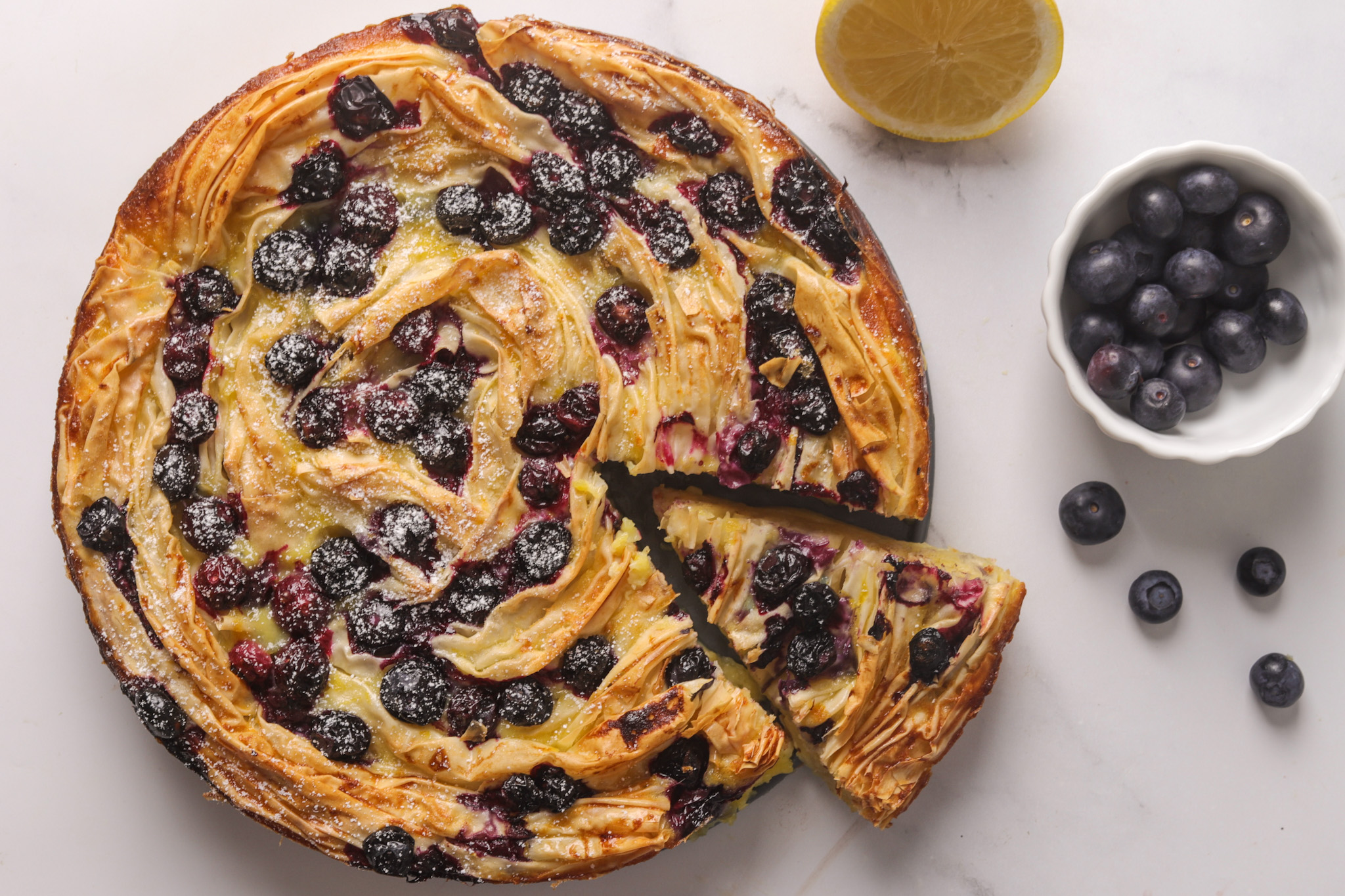 Rustic golden filo pastry soufflé filled with lemon custard and fresh blueberries, dusted with icing sugar