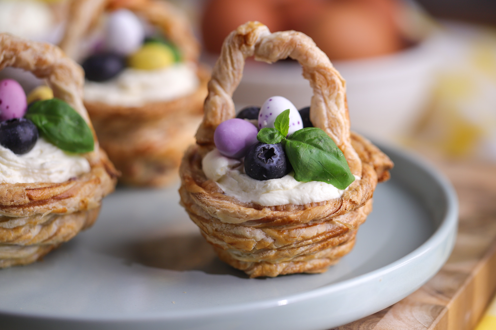 Crispy golden pastry baskets filled with jammy blueberry and peach compote, piped with whipped cheesecake cream and topped with fresh blueberries and mini chocolate Easter eggs.