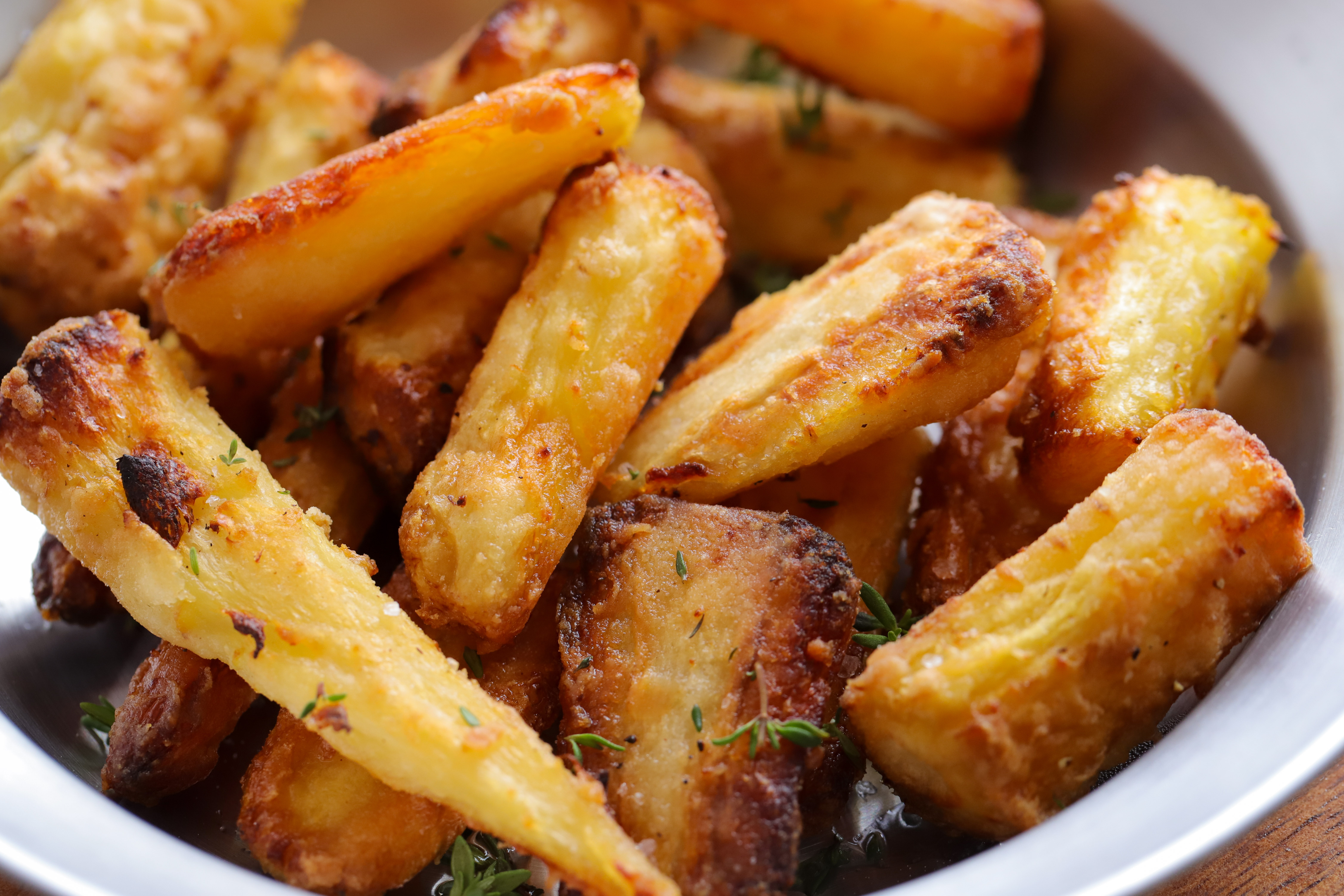 Golden, crispy roasted parsnips on a baking tray, sprinkled with fresh thyme and flaky salt.