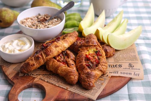 Golden flaky croissants stuffed with baked egg, red capsicum and crumbled feta, served warm on a wooden board