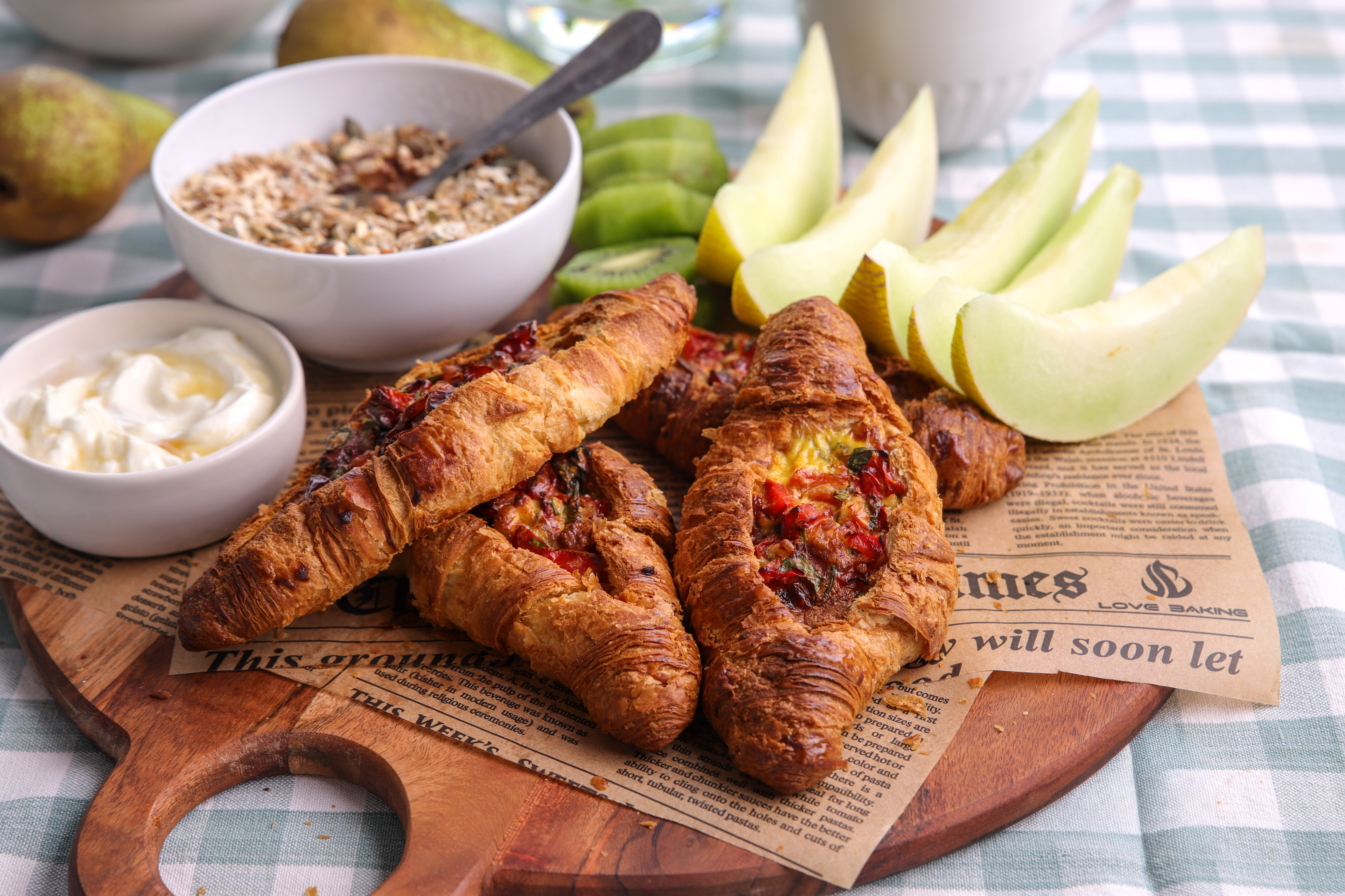 Golden flaky croissants stuffed with baked egg, red capsicum and crumbled feta, served warm on a wooden board