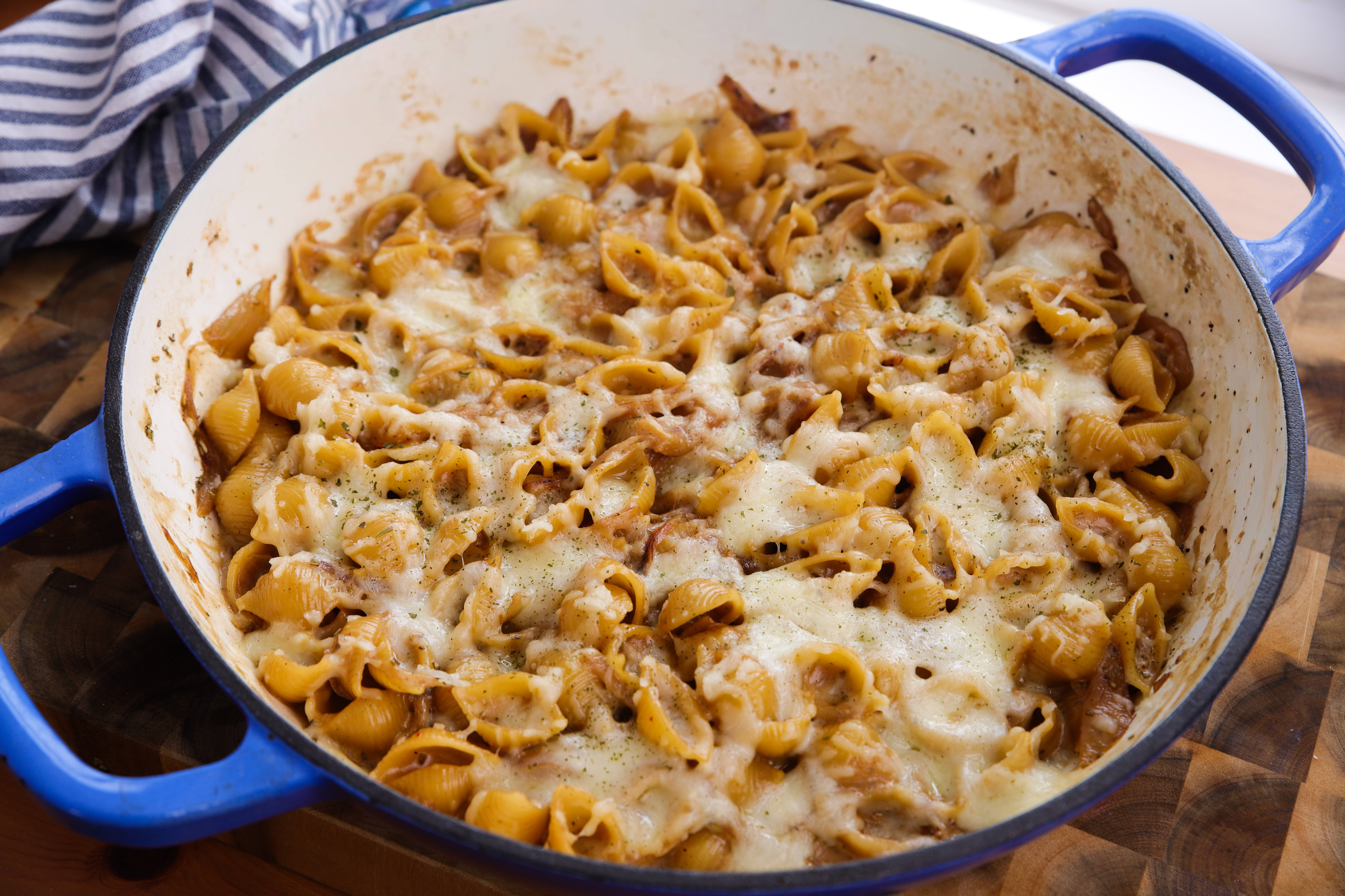 A deep pan of creamy French onion pasta topped with golden, bubbling gruyère, fresh from the grill, with a ladle resting on the side