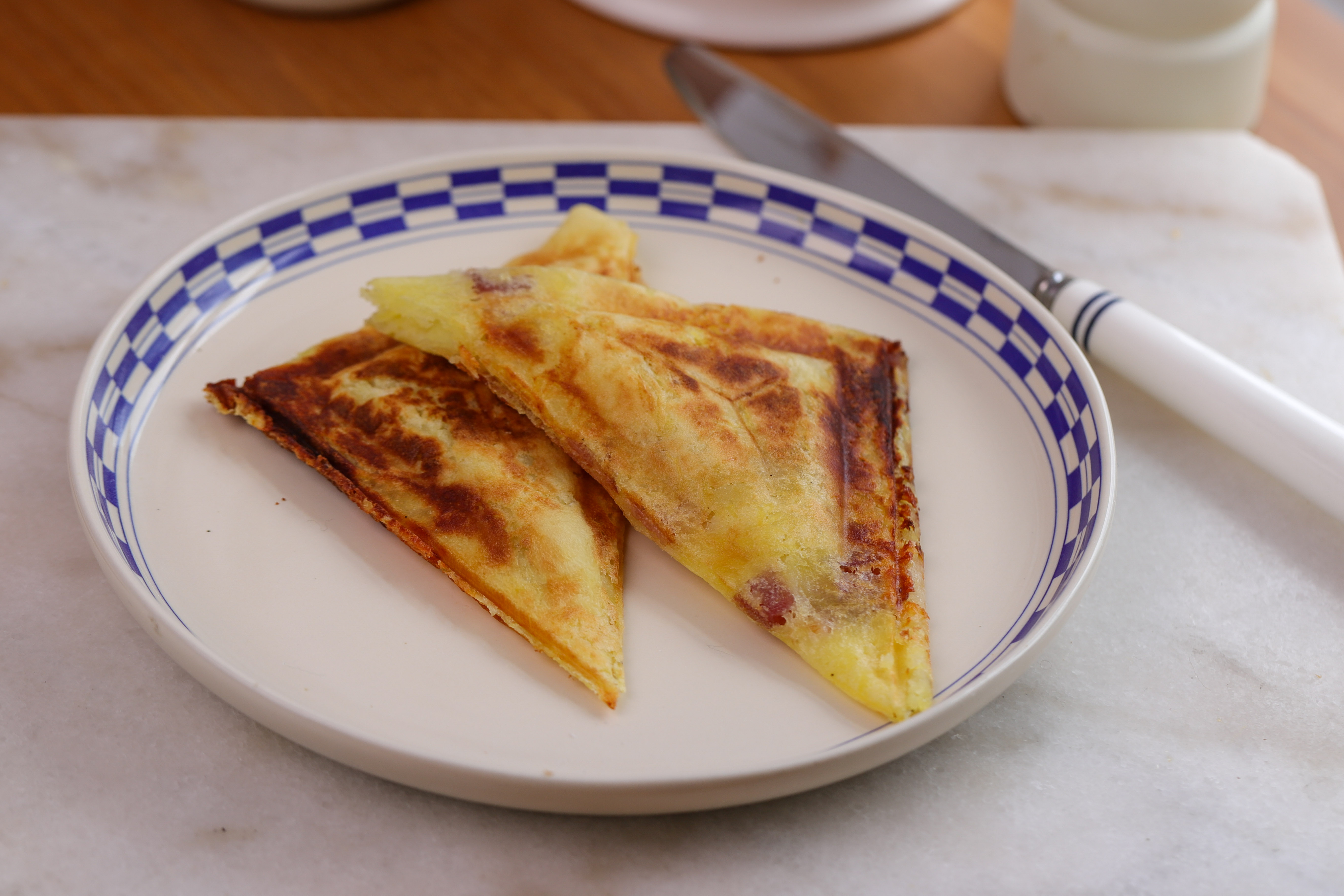 Golden crispy mashed potato toastie cut in half on a wooden board, oozing melted cheese with a golden crust