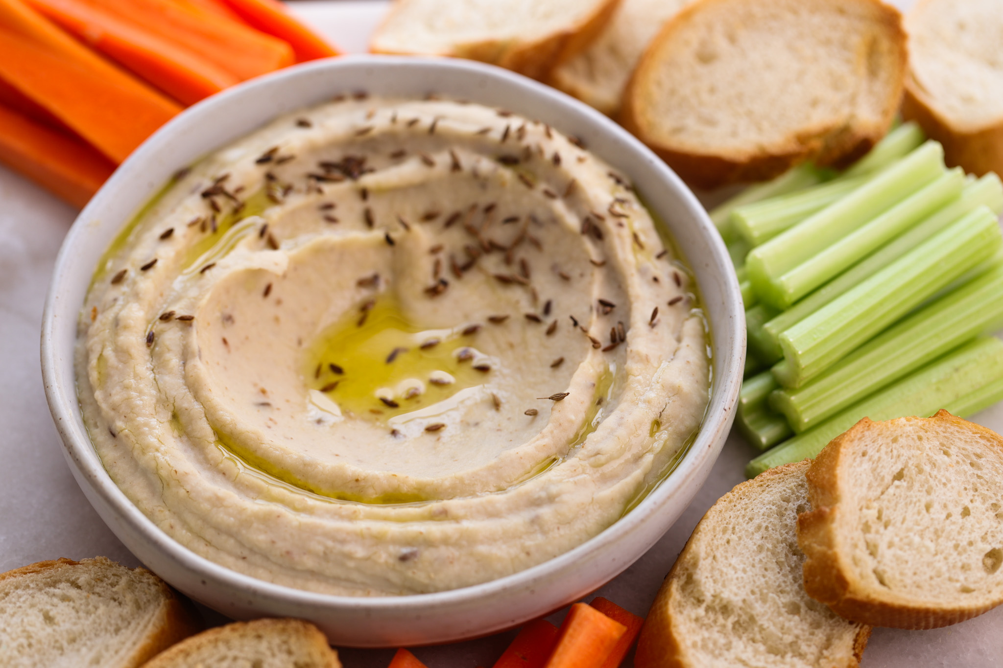 Creamy parsnip and butter bean hummus in a shallow bowl, drizzled with olive oil and dusted with paprika, served with cucumber sticks, celery, carrots, and crackers