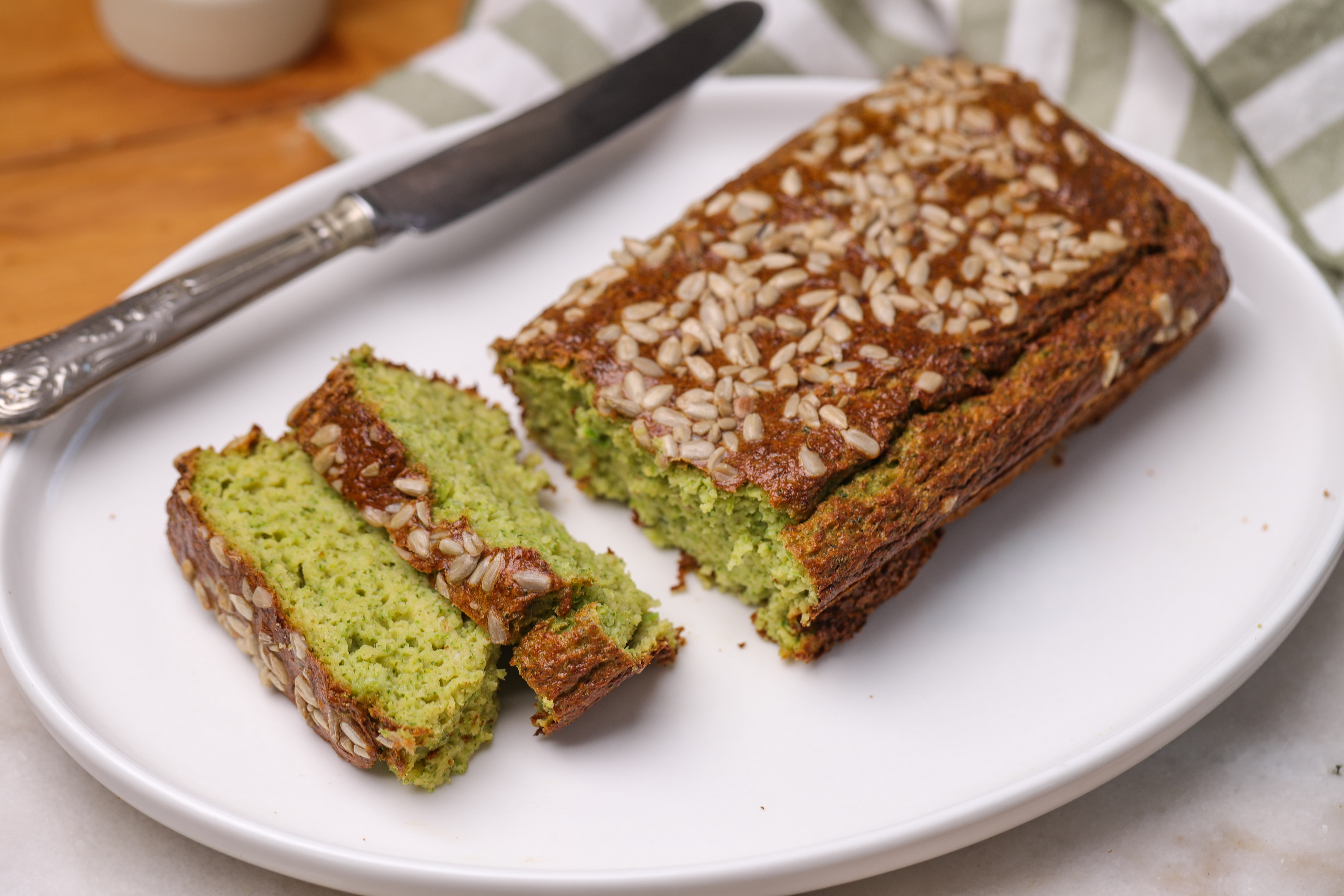Golden broccoli bread loaf topped with mixed seeds, sliced to show a soft, green-flecked crumb