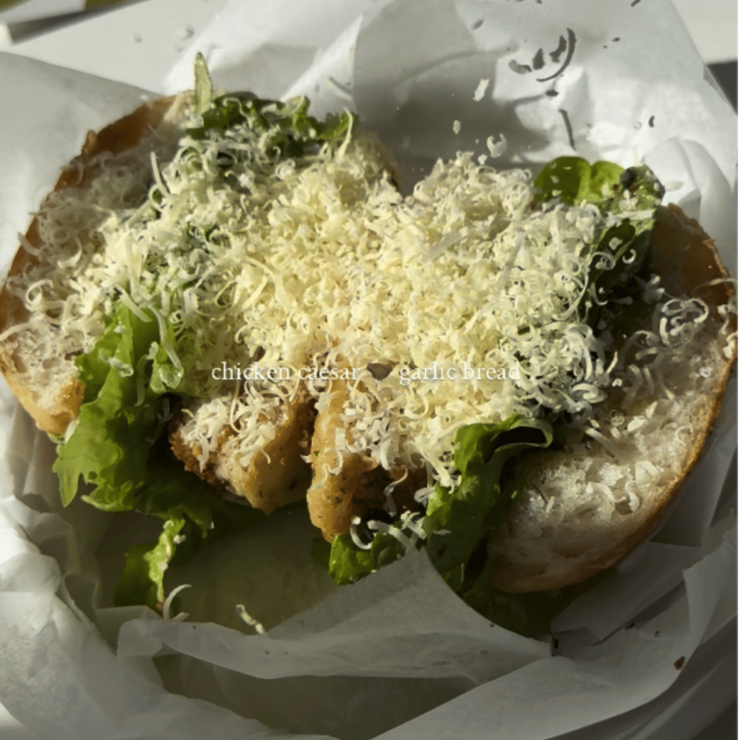 Crispy panko chicken Caesar sandwich in toasted garlic focaccia, layered with shredded cos lettuce and grated Parmesan, cut in half on a board.
