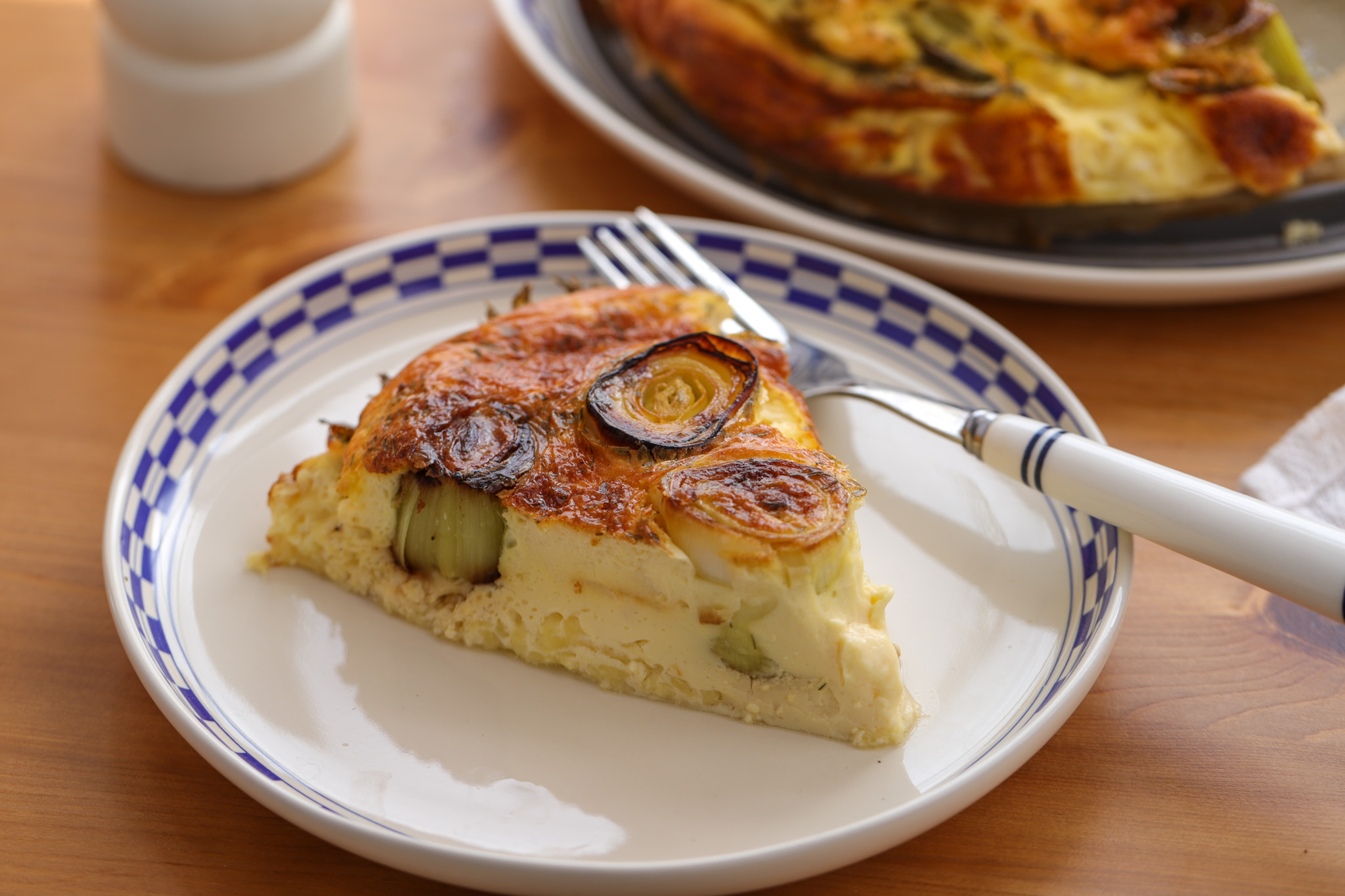 Sliced crustless leek quiche in a round dish, showing a golden top and creamy, cheese-flecked egg filling