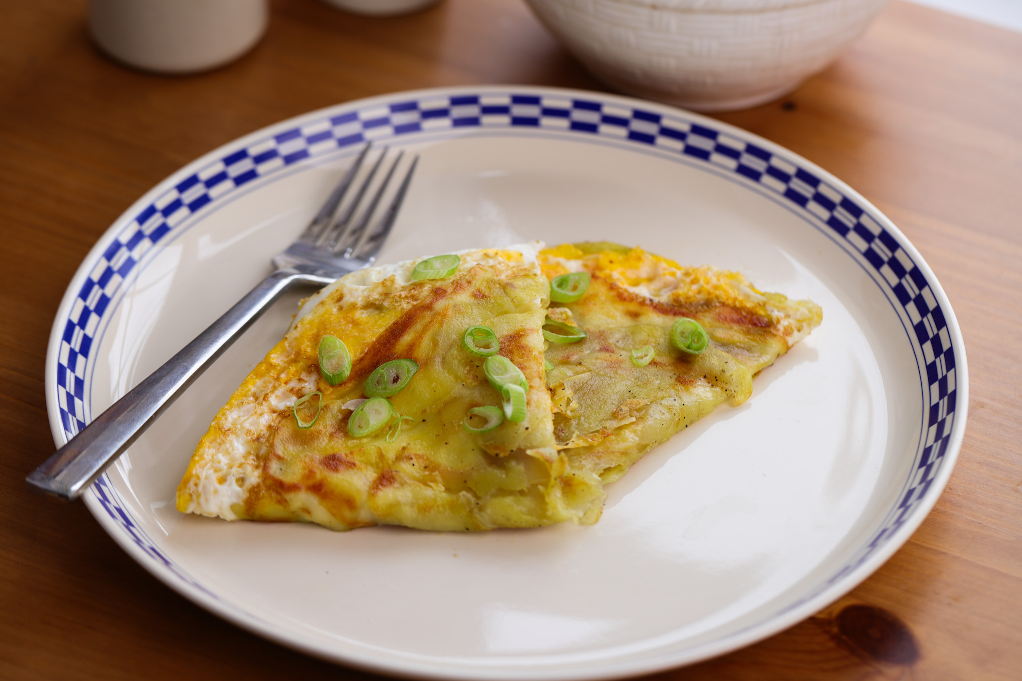 Crispy golden potato ribbons topped with a folded cheesy egg omelette on a white plate
