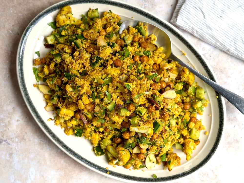 Golden roasted cauliflower florets and crisp chickpeas folded through turmeric-yellow couscous, scattered with flaked almonds, nigella seeds and chopped parsley and mint.