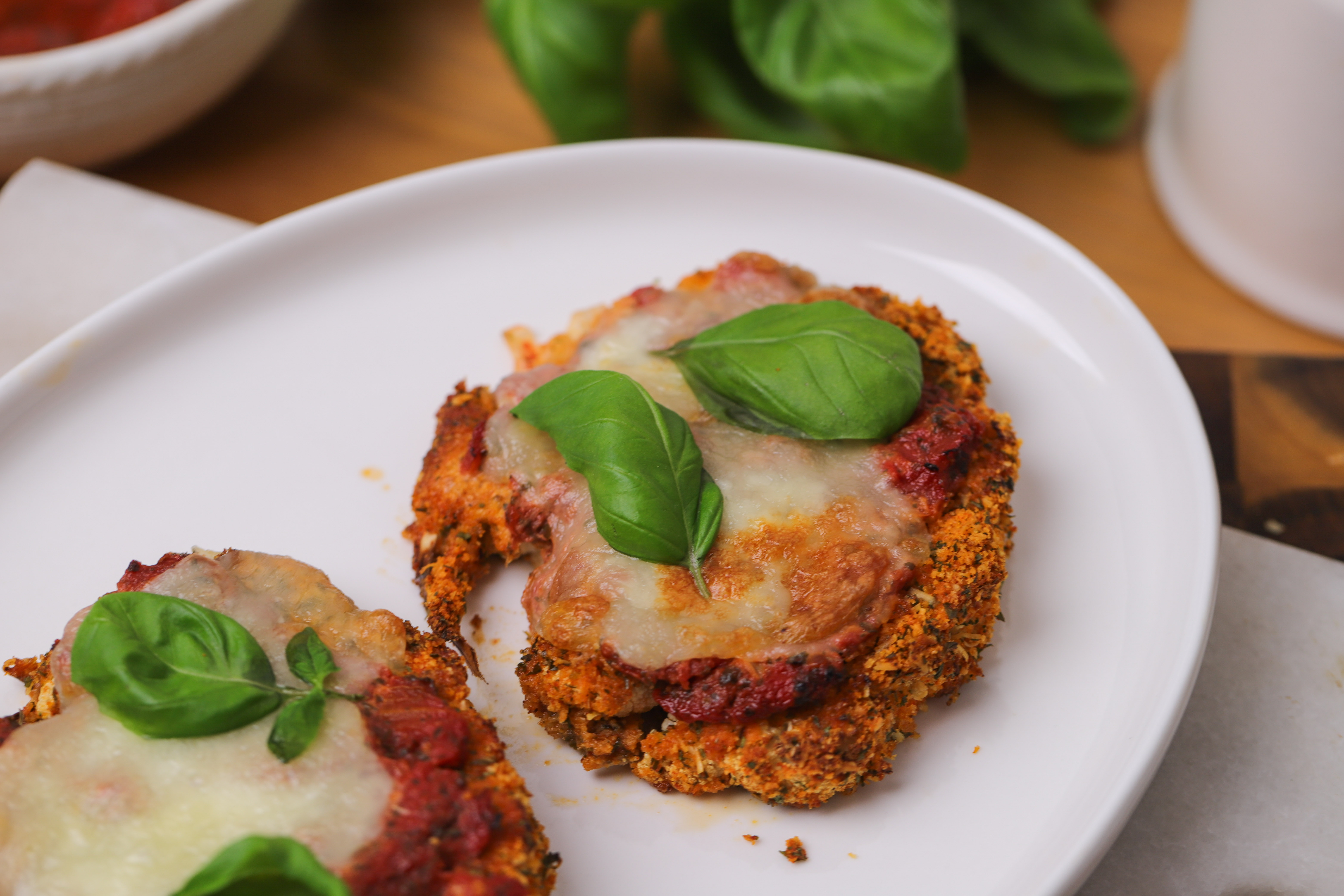 Golden, crumbed cauliflower steaks topped with tomato sauce and melted mozzarella in a baking dish