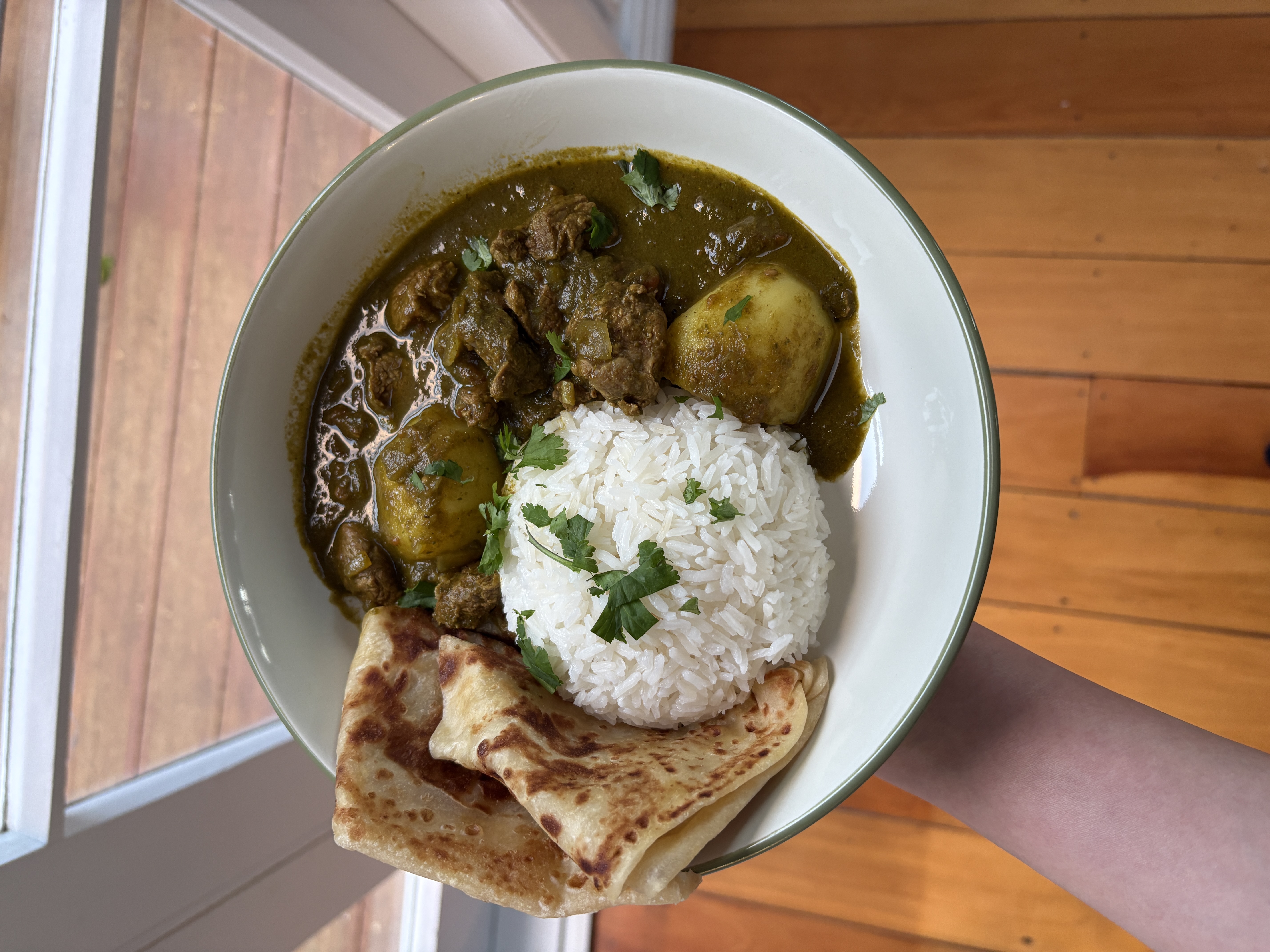 Lamb and spinach curry in a bowl, with tender chunks of lamb and potato in a green coconut and coriander sauce, topped with fresh coriander and served with rice and naan