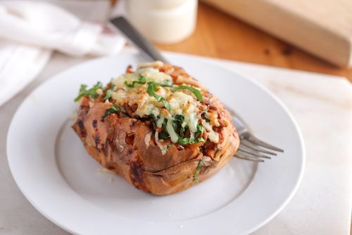 Baked orange kumara split open and filled with paprika beef mince and wilted spinach, topped with golden melted cheese on a baking tray