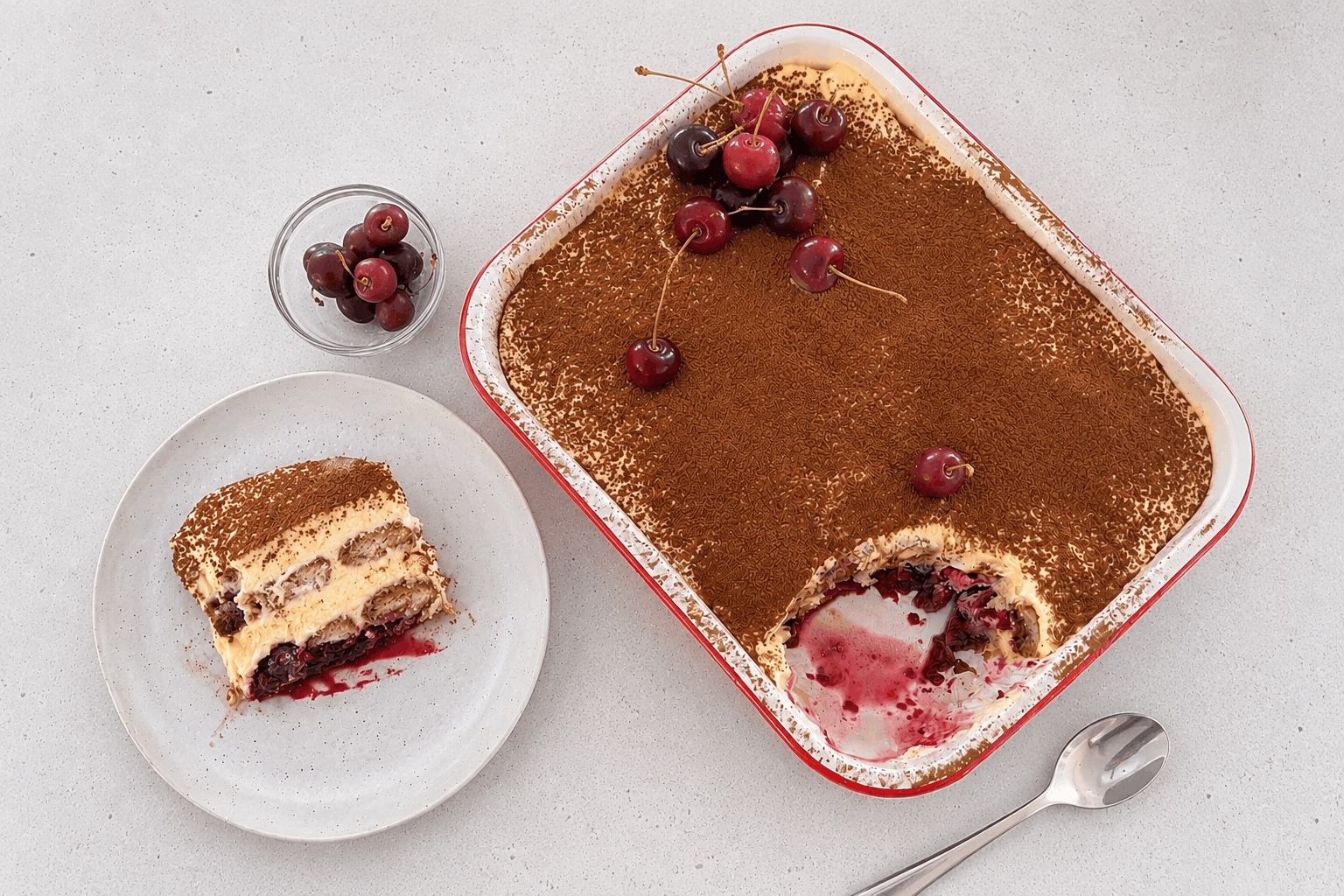 Glass dish layered with coffee-soaked ladyfingers, vibrant cherry compote, and fluffy mascarpone cream, dusted with cocoa and topped with fresh cherries.