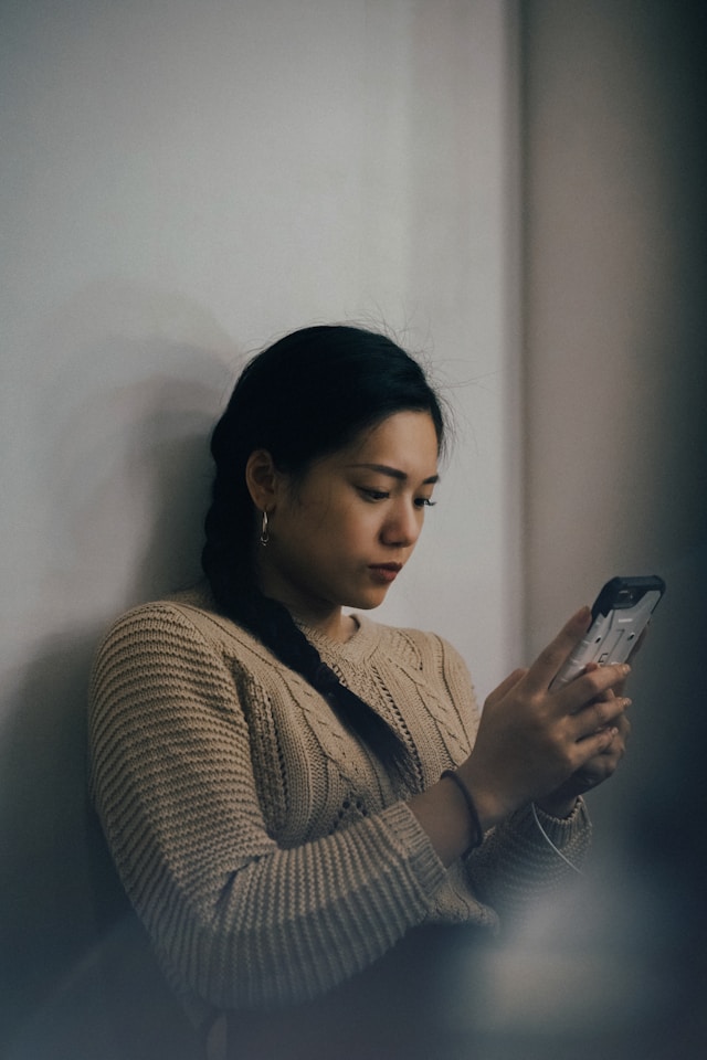 A woman checking her phone while leaning against a wall