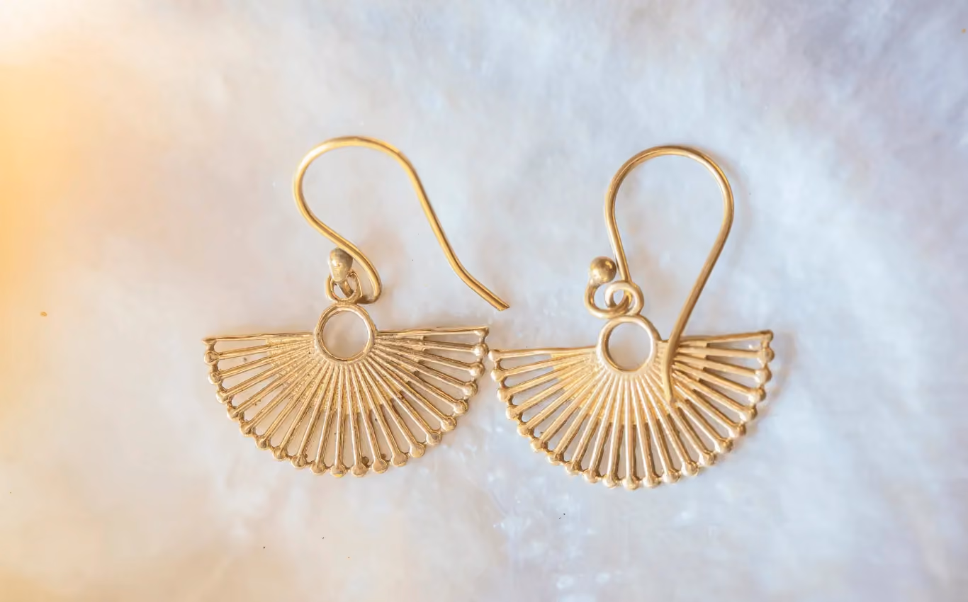 Pair of gold fan-shaped dangle earrings with fine rod detailing on a soft white surface.