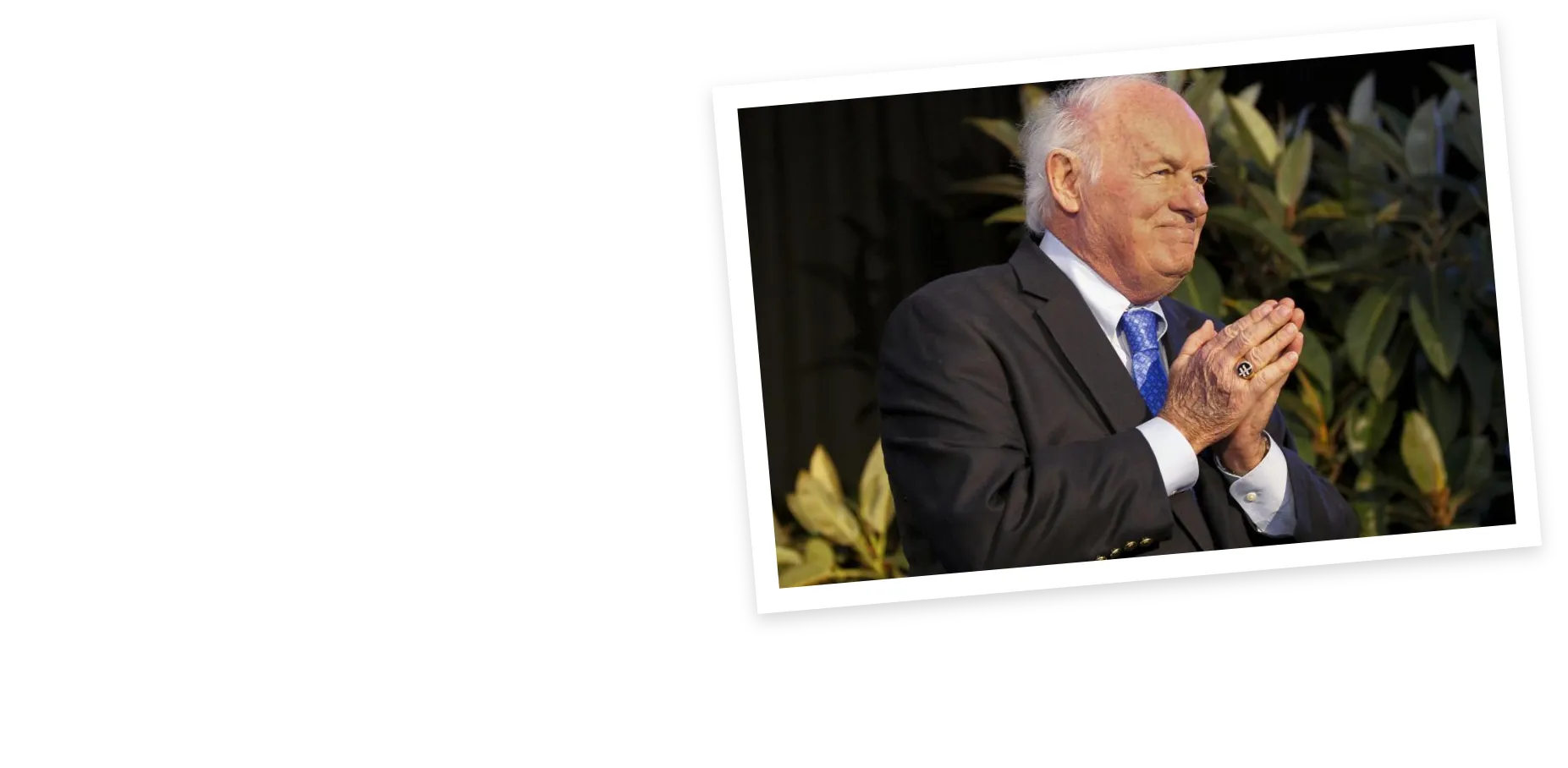 Denny Sanford smiling with his hands clasped in appreciation during a public event.