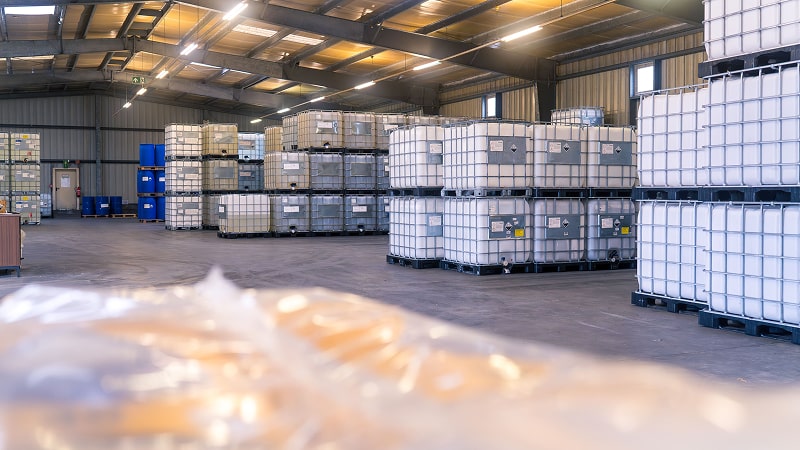 Industriehalle der Imhoff & Stahl GmbH mit zahlreichen weißen IBC-Containern, geordnet auf Paletten und gestapelt bis zur Decke.