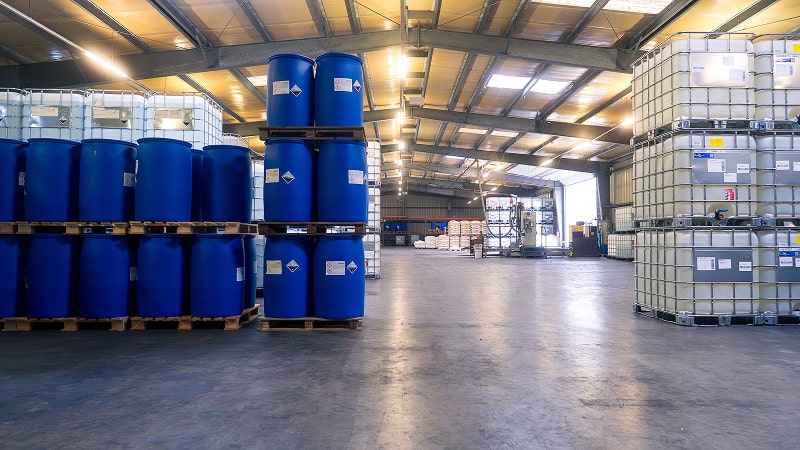 Offene Lagerfläche der Imhoff & Stahl GmbH mit zentral gestapelten blauen Kunststofffässern, umgeben von IBC-Containern.