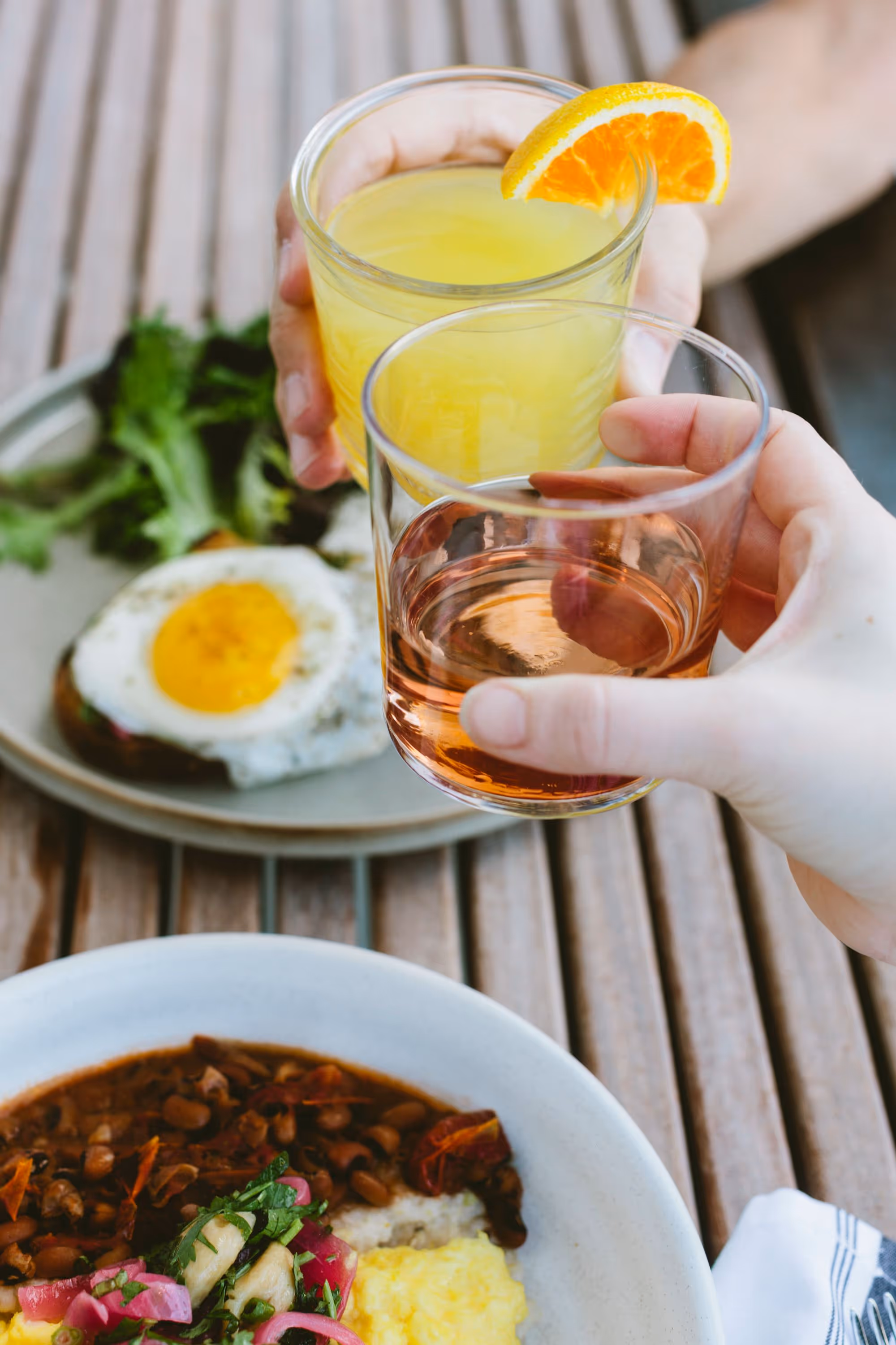 hands holding drinks over a table with food