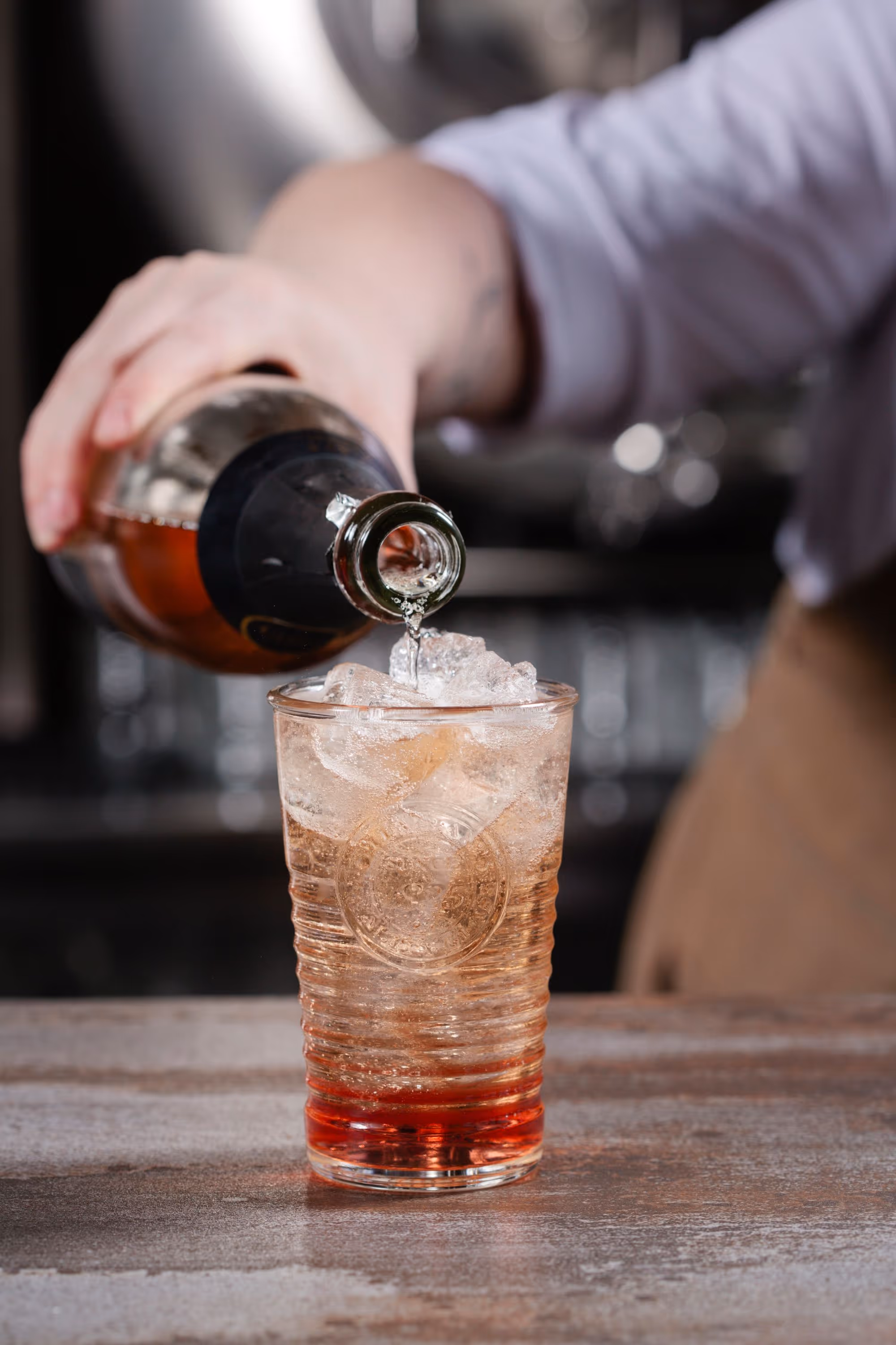 hand pouring sparkling beverage into glass with ice