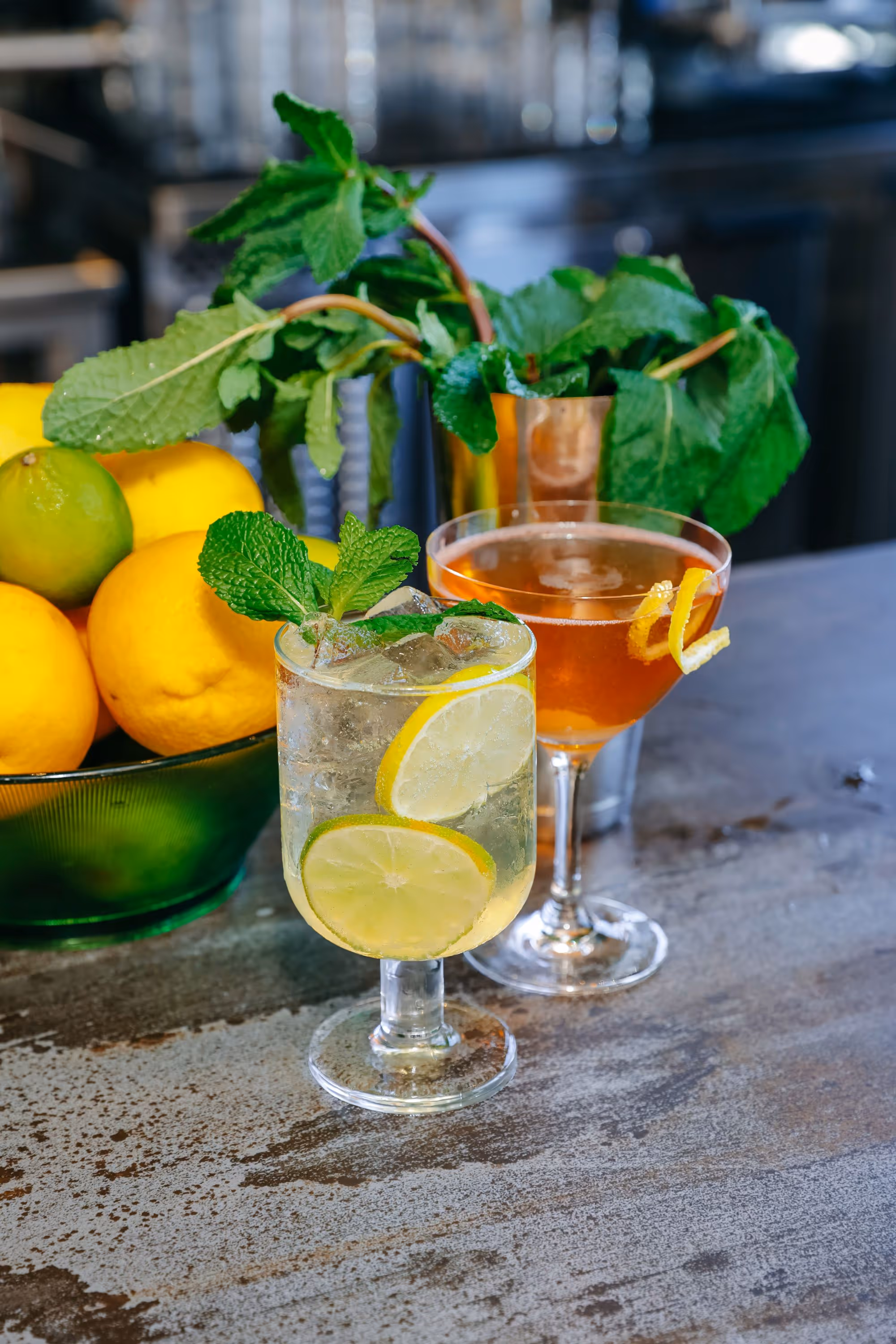 two cocktails with fruit and mint in background