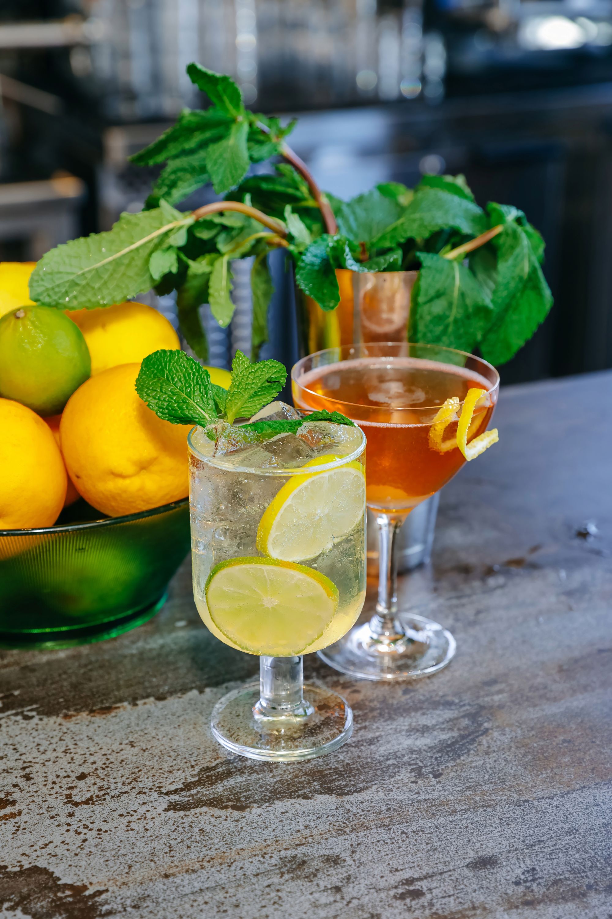 two cocktails with fruit and mint in background