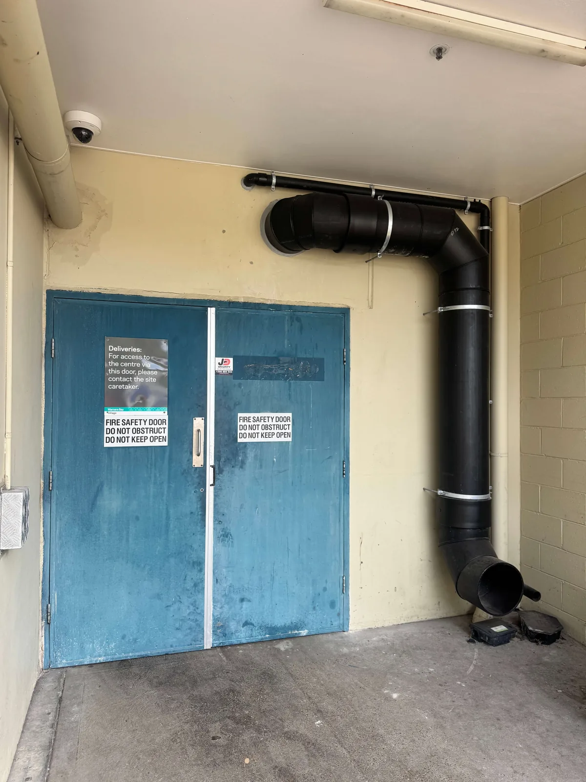 Siphonic drainage at John St, Warners Bay — new external downpipe run installed beside the loading dock fire door
