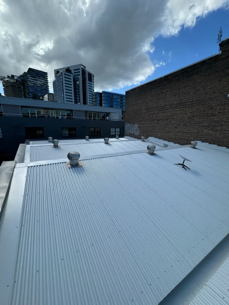 Metal roof replacement at Henrietta St, Chippendale — completed roof with new whirlybird ventilators against the city skyline