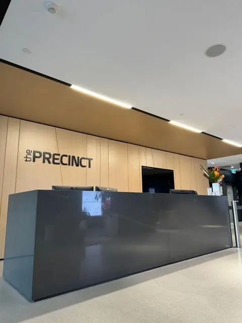 Fit out at Precinct Co-Working, Olympic Park — timber-panelled reception desk with Precinct signage