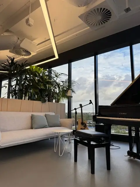 Office fit out at Precinct Co-Working, Olympic Park — breakout lounge with piano and city outlook