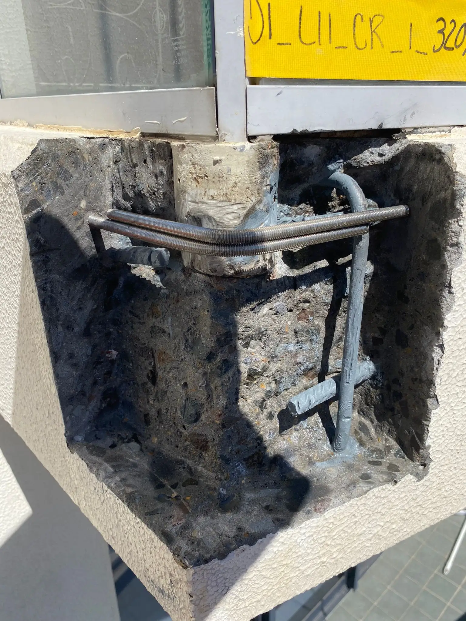 Concrete spalling repair at Sergeants Lane, St Leonards — broken-out spall exposing corroded reinforcement bars before treatment