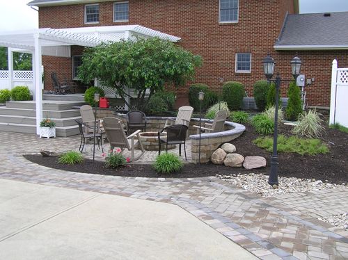 Brick home patio with seating, paver walkways, trimmed shrubs, and a landscaped planting bed.