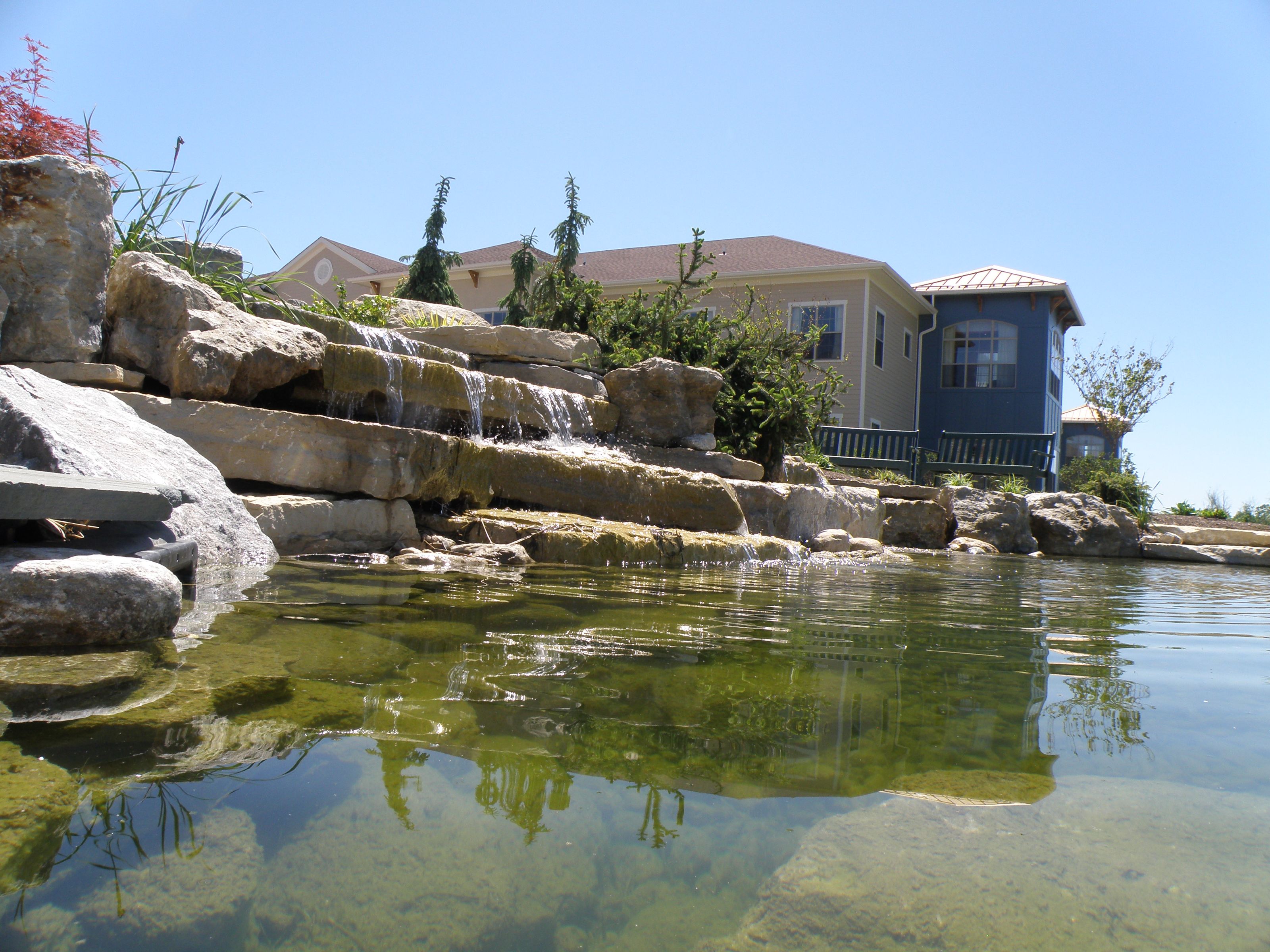 Rock waterfall flowing into a landscaped pond beside a building