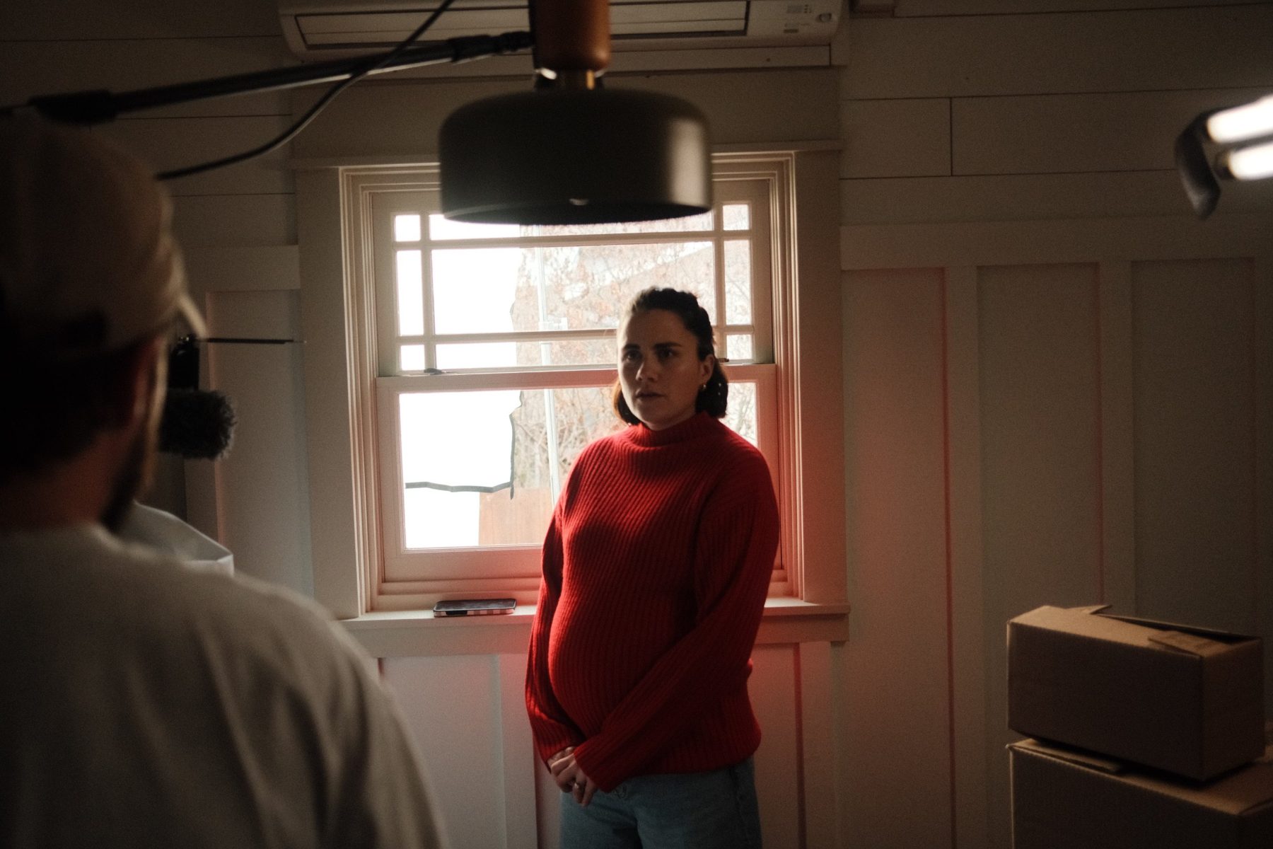 Behind the scenes: the mother in her red sweater by the window between takes