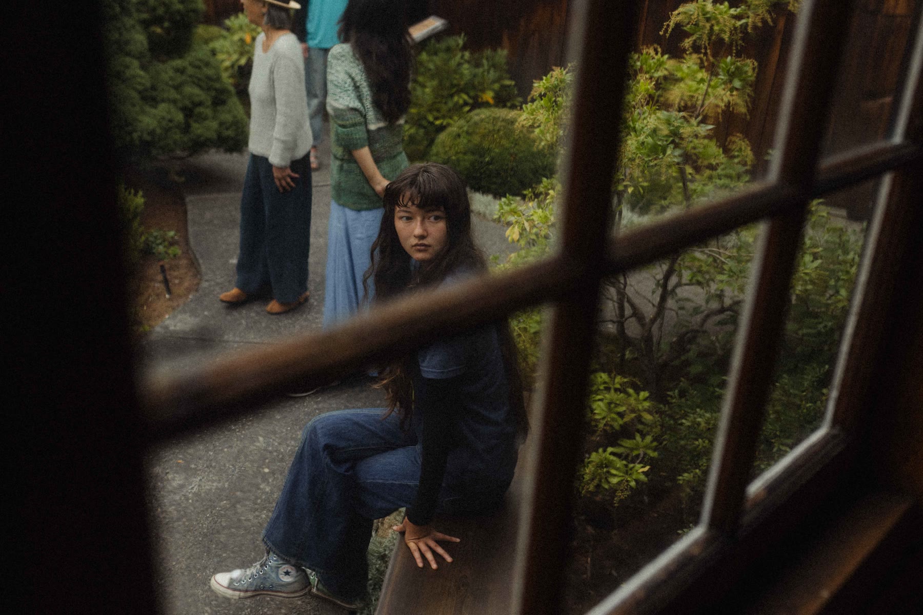 A visitor on a garden bench, seen through a wooden window frame