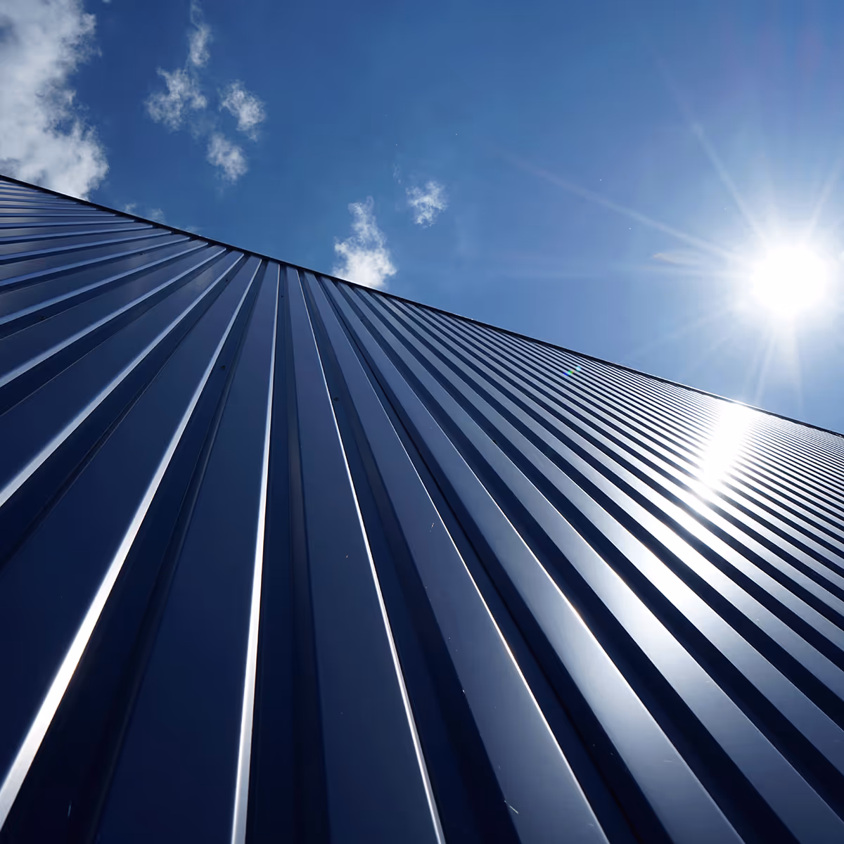 Close-up view of a sleek metal roof with clean lines set against a bright blue sky. The image showcases the aesthetic and durability of modern roofing materials.