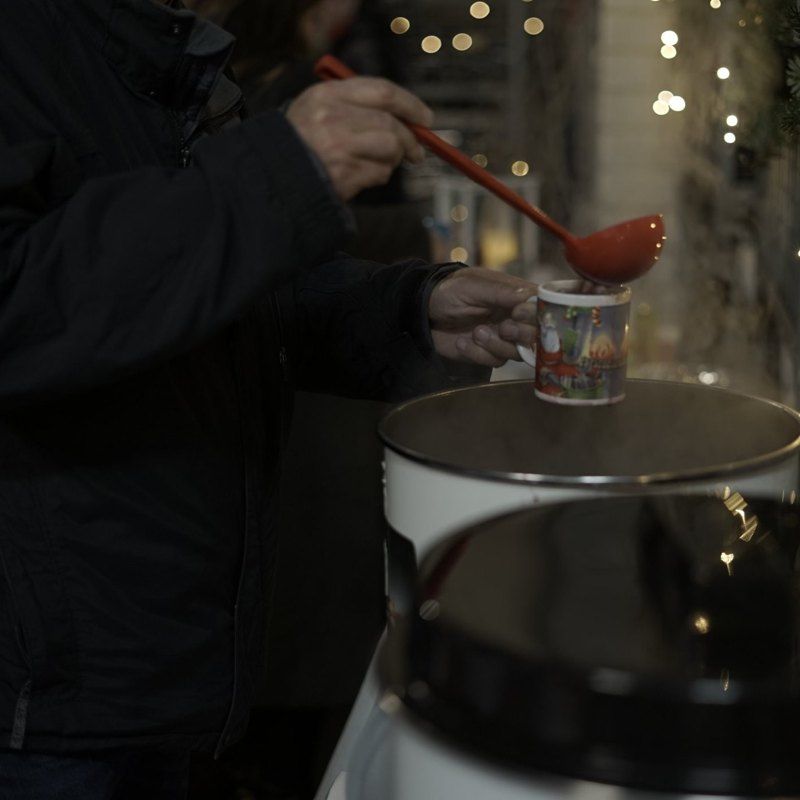 Glühwein wird aus dem Topf in eine Weihnachtstasse geschöpft