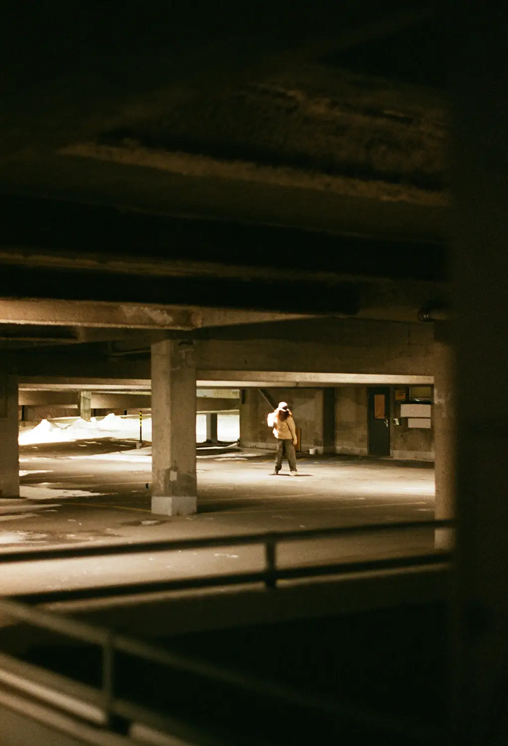 Person standing alone in a dimly lit concrete parking garage at night.