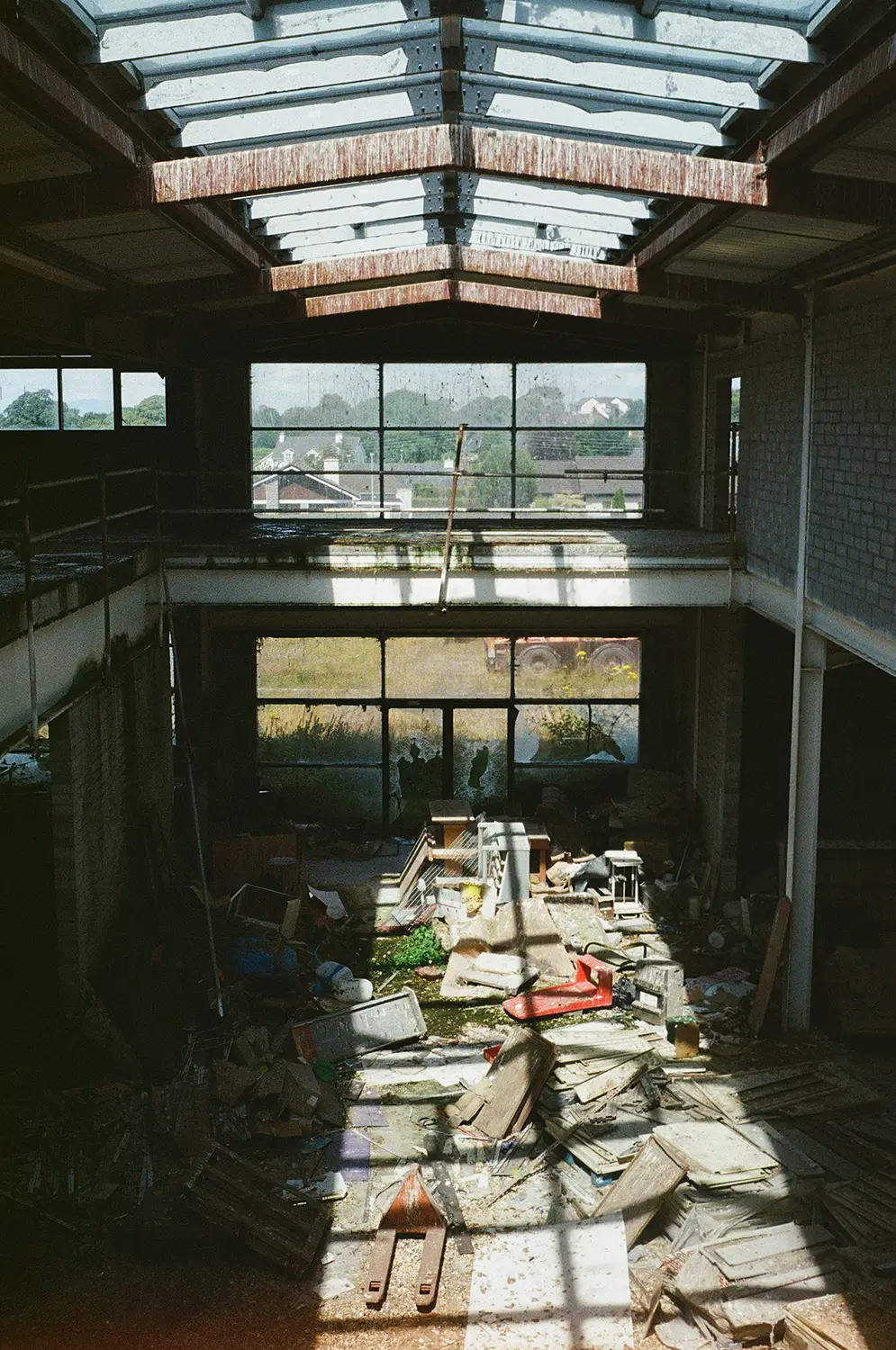 Interior of an abandoned warehouse cluttered with debris and old equipment under a rusted skylight roof.