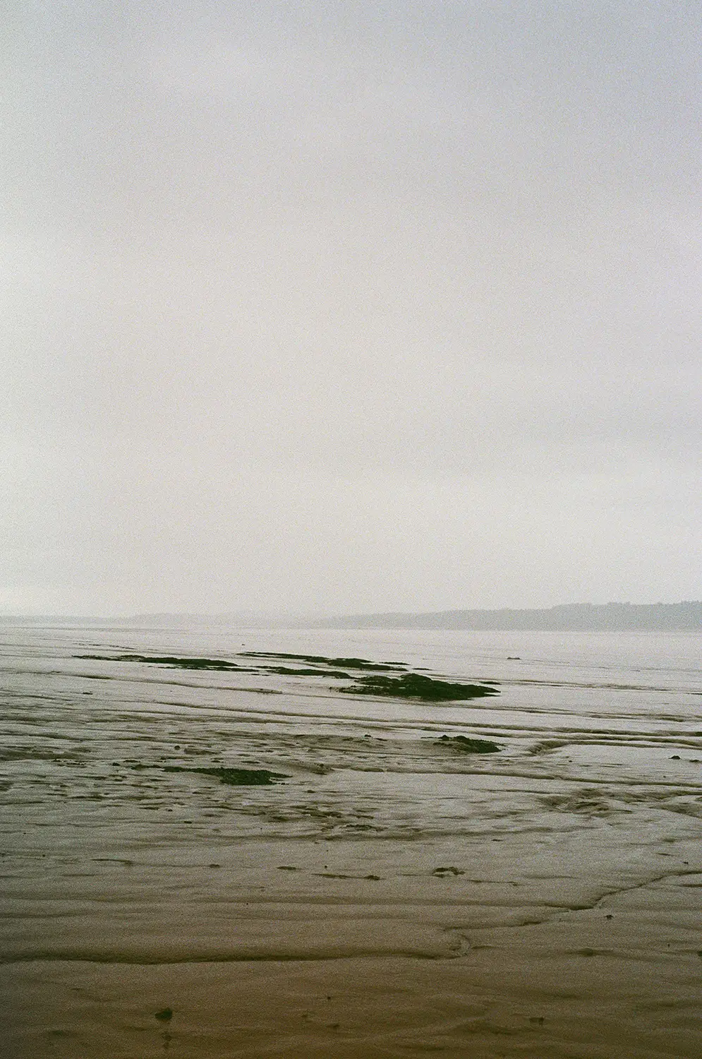 Overcast sky above a vast, wet sandy beach with shallow water and distant shoreline.