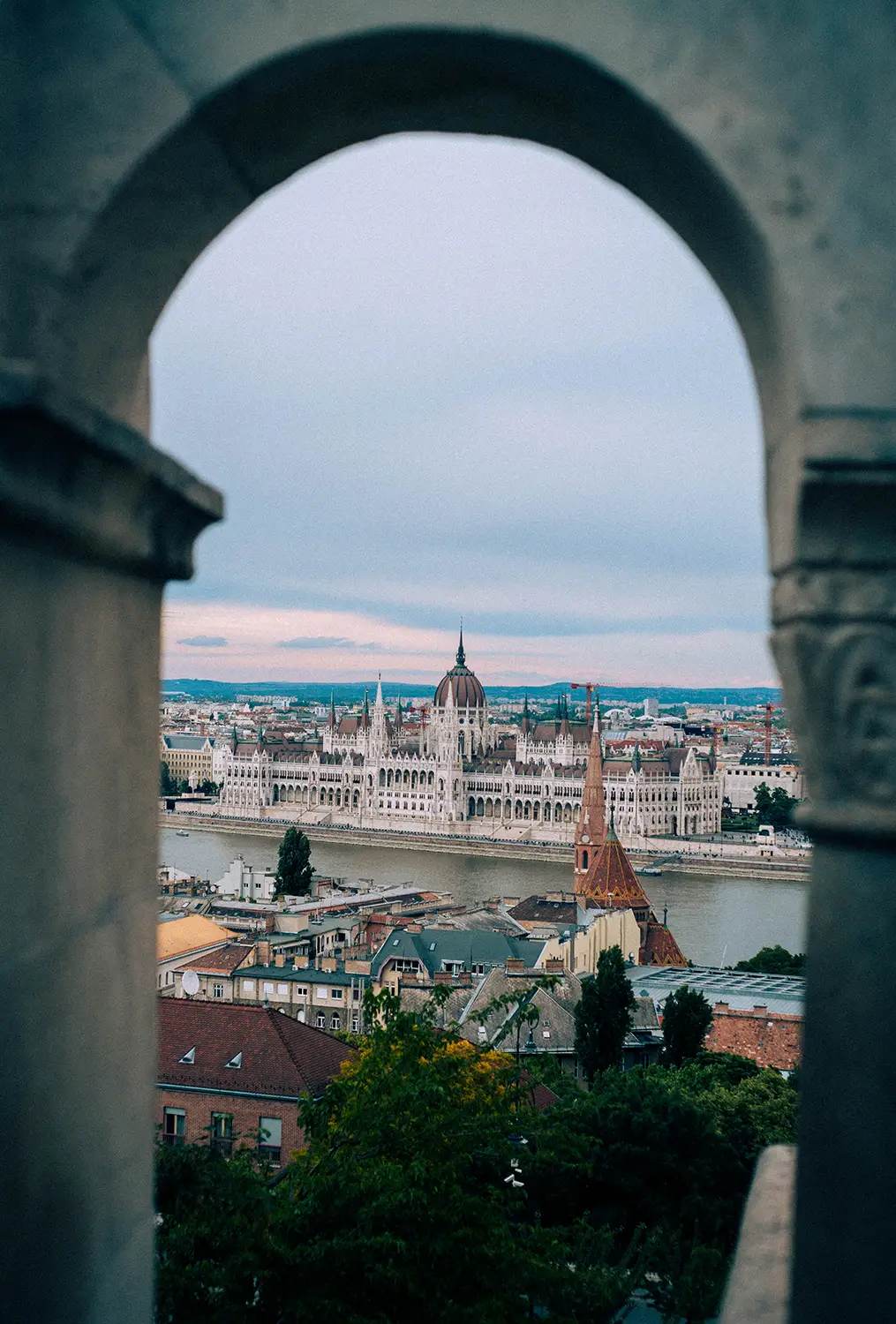 View of the Hungarian Parliament building across the Danube River framed by a stone archway.