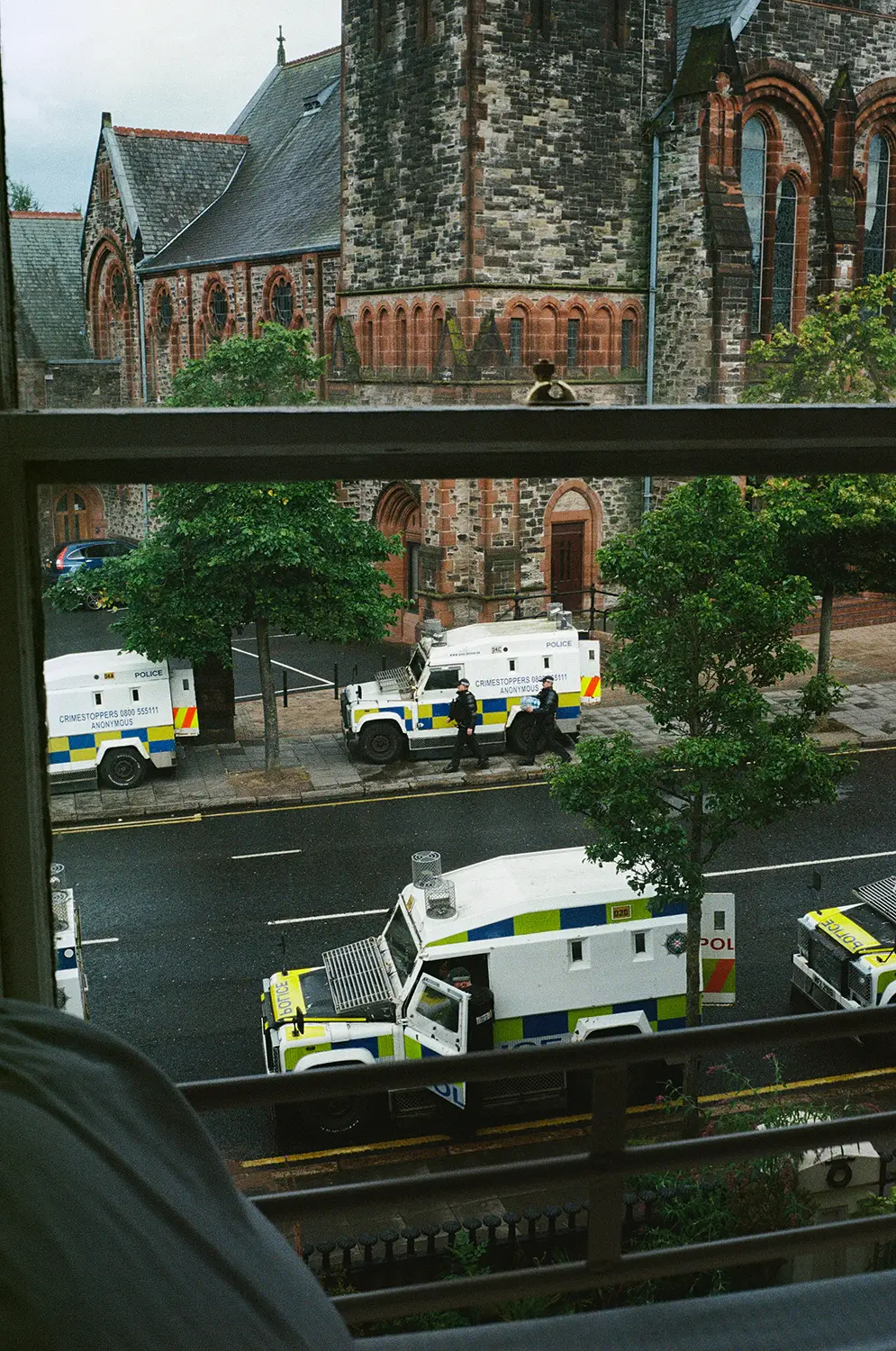 View through a window of police armored vehicles and officers on a street next to an old stone church.