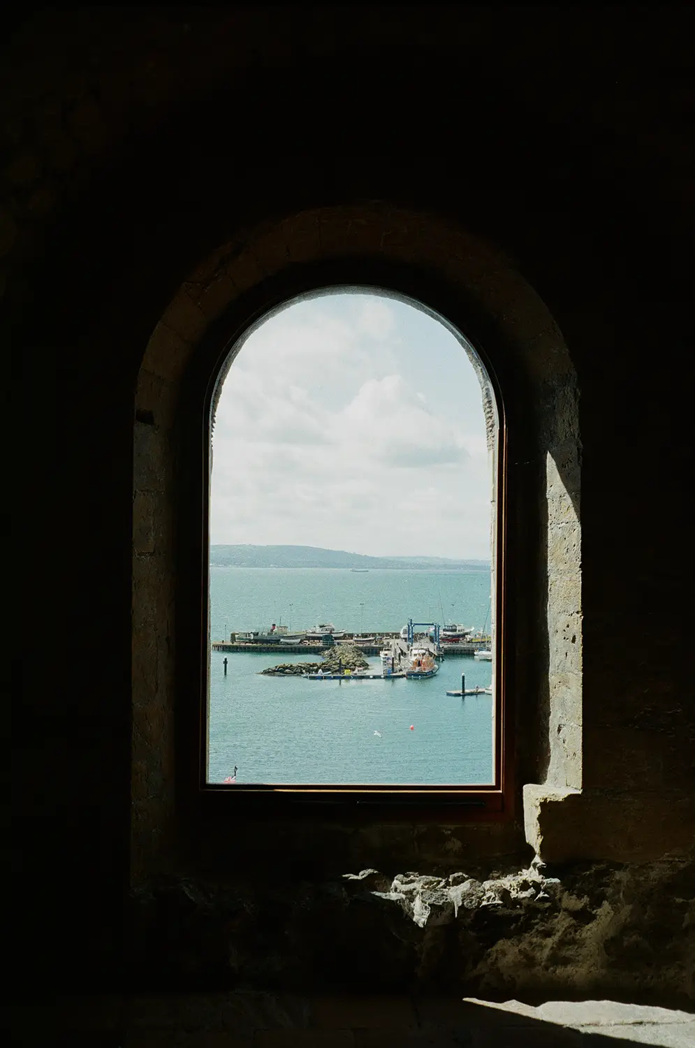 View of a harbor with boats and a pier seen through a stone arched window.