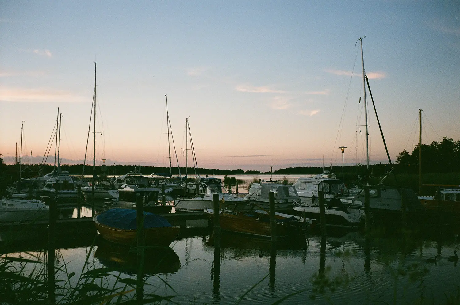 Harbor at dusk with multiple docked boats and calm water reflecting the sunset sky.