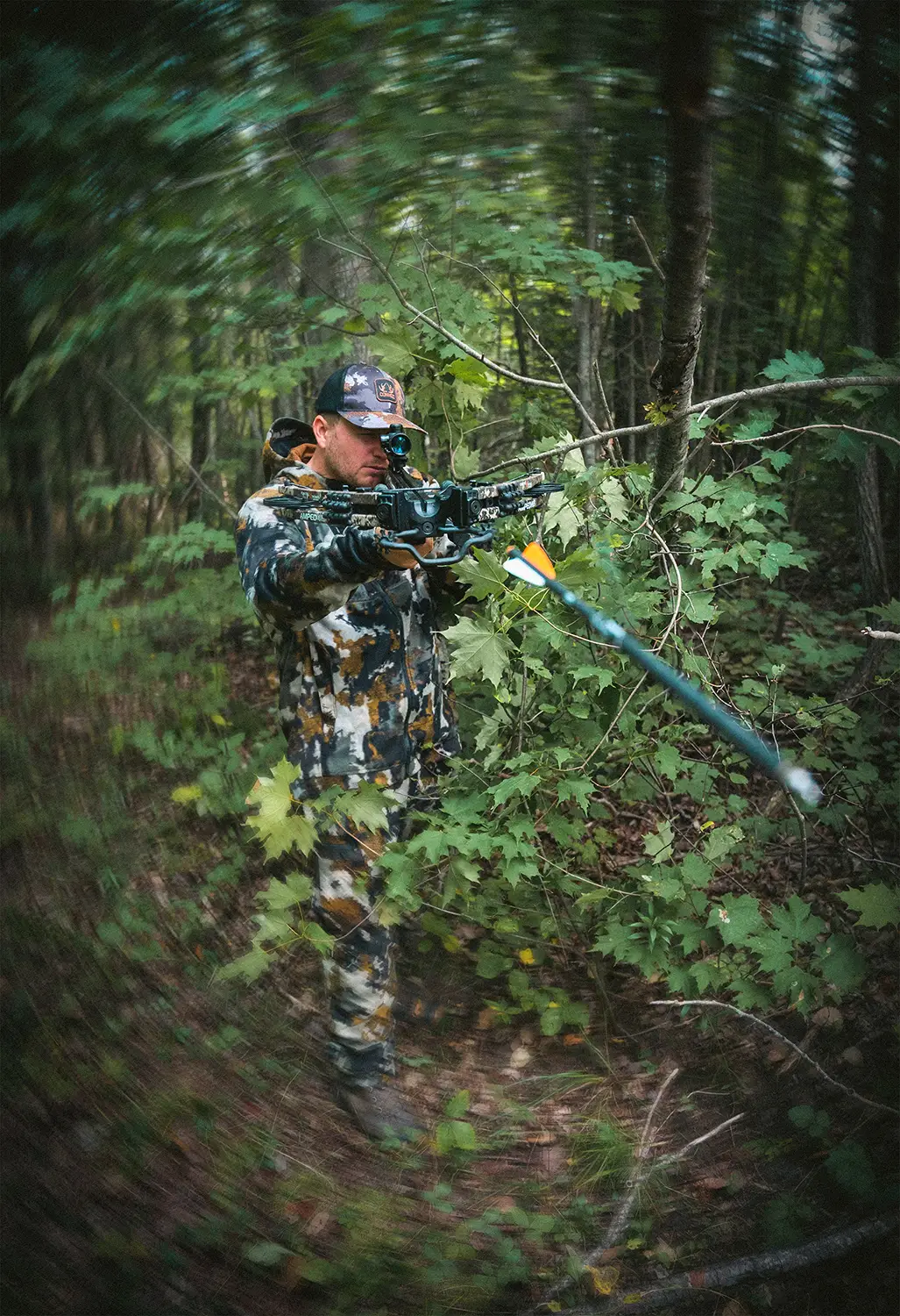 Man in camouflage clothing aiming a crossbow with an arrow in a dense forest.