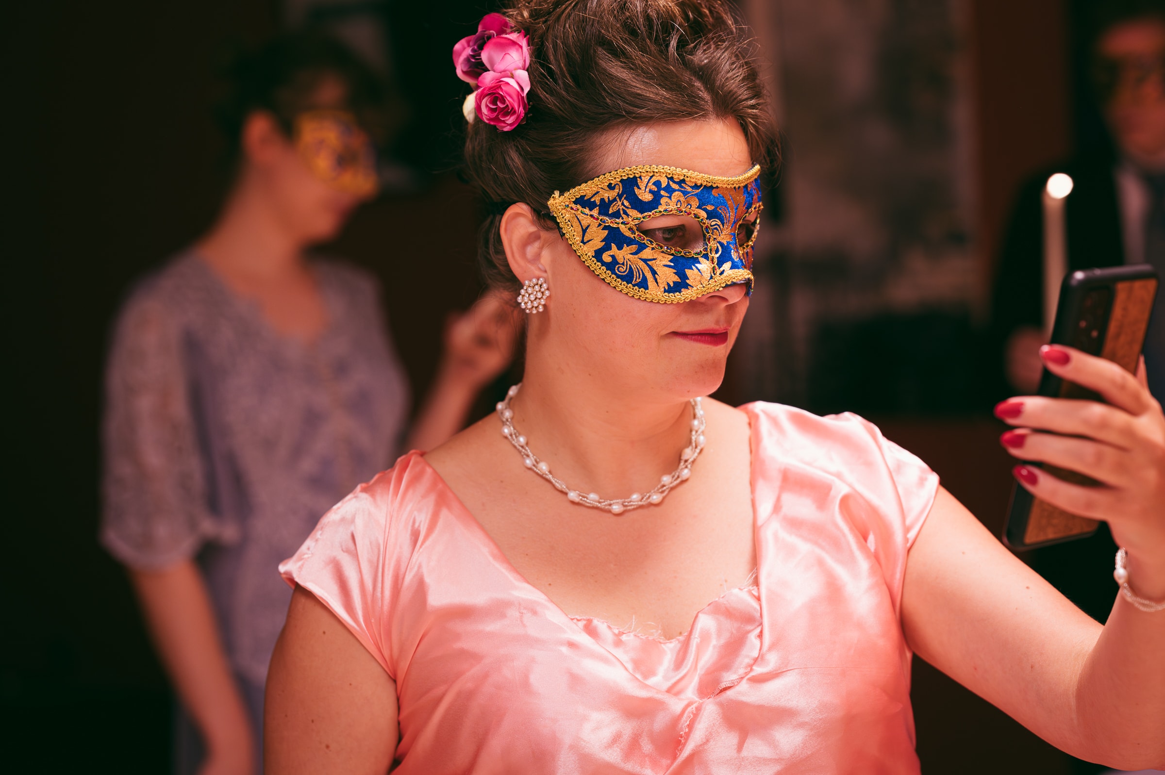 Woman in masquerade mask and gown looking at phone