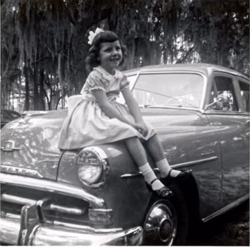 Brenda Hensel as a young girl sitting on her parents' car.