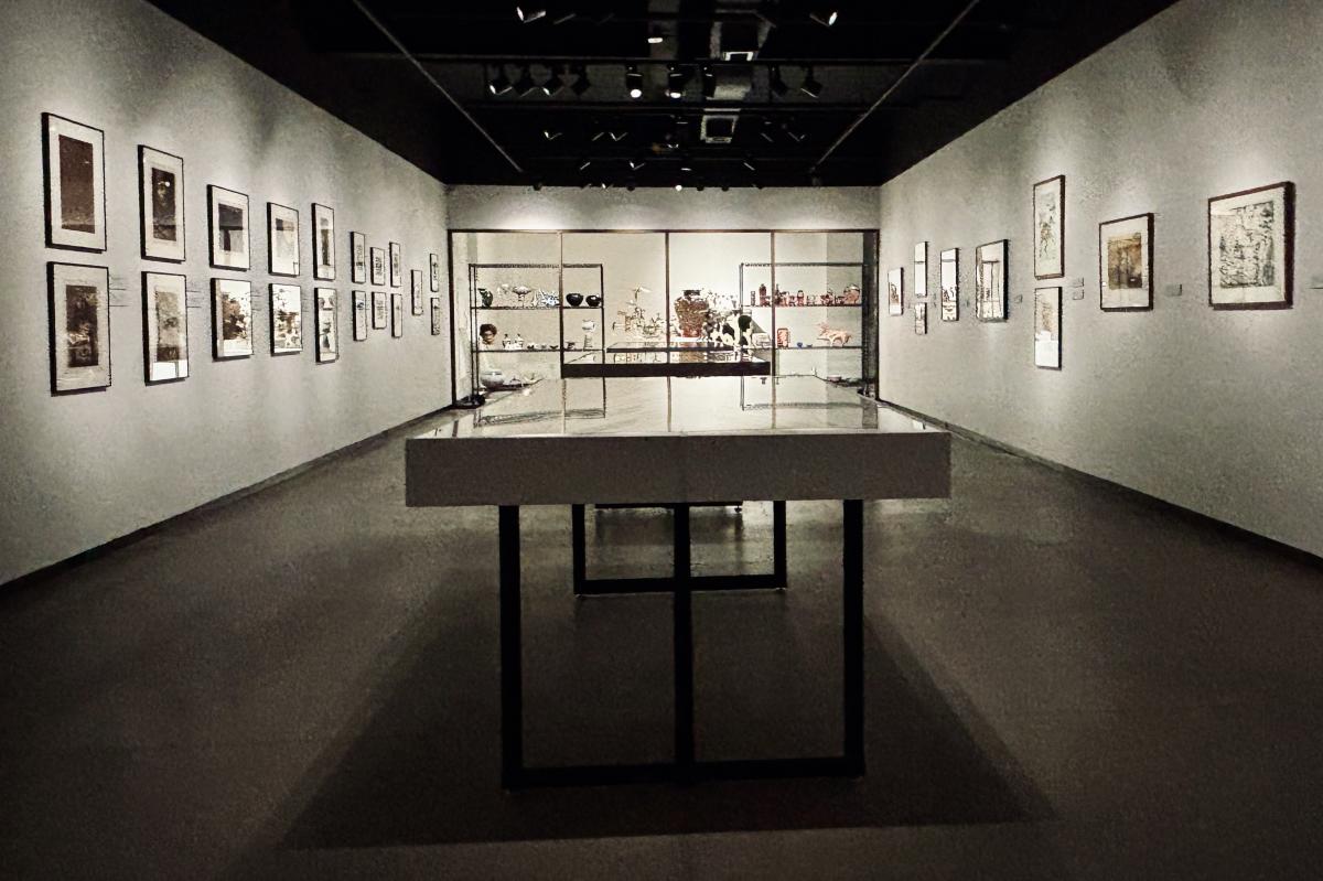 Interior of a dimly lit art gallery featuring multiple framed artworks on the walls and glass displa…