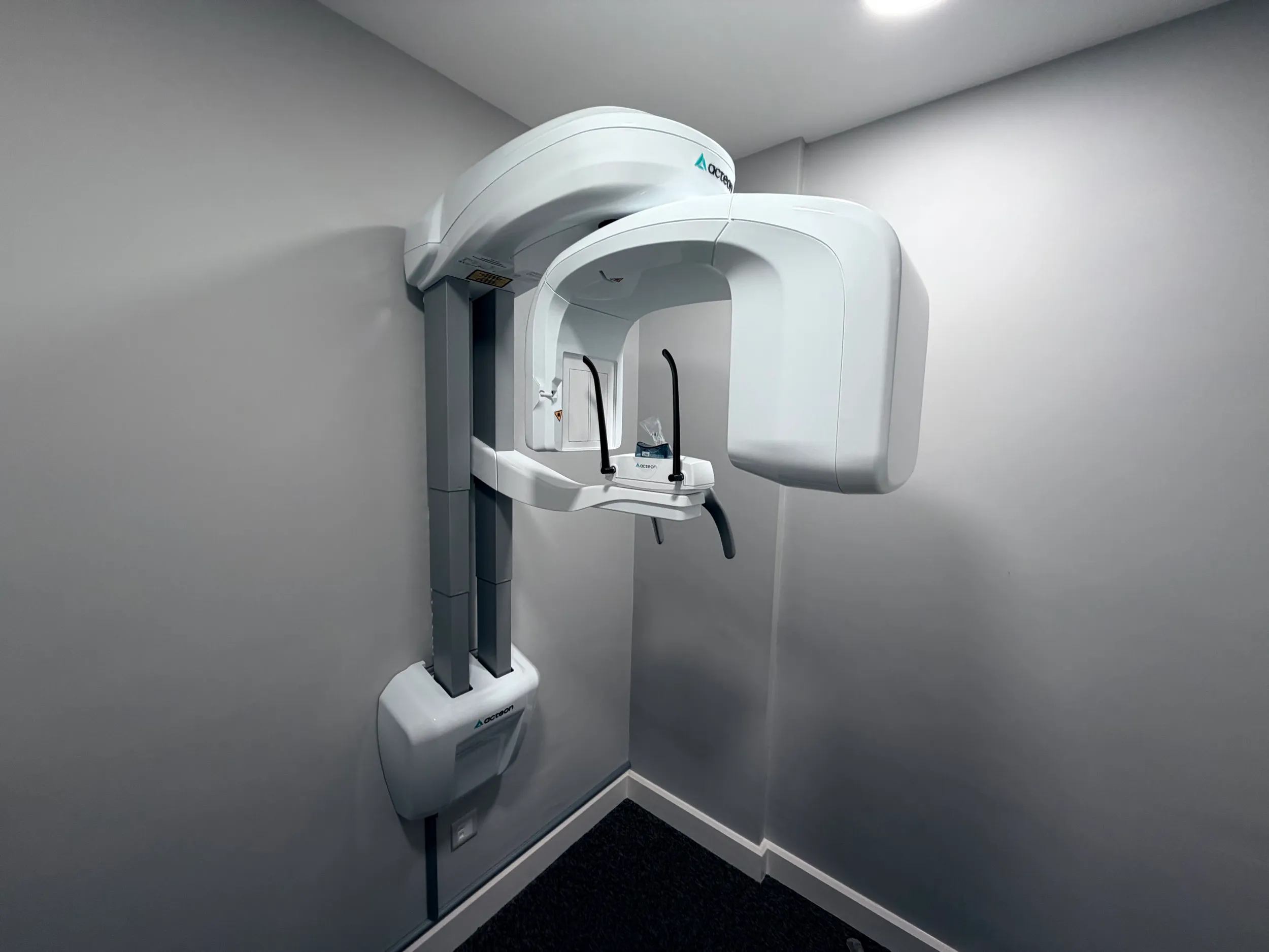 White Acceon dental panoramic X-ray machine mounted on a corner wall in a clinical room.